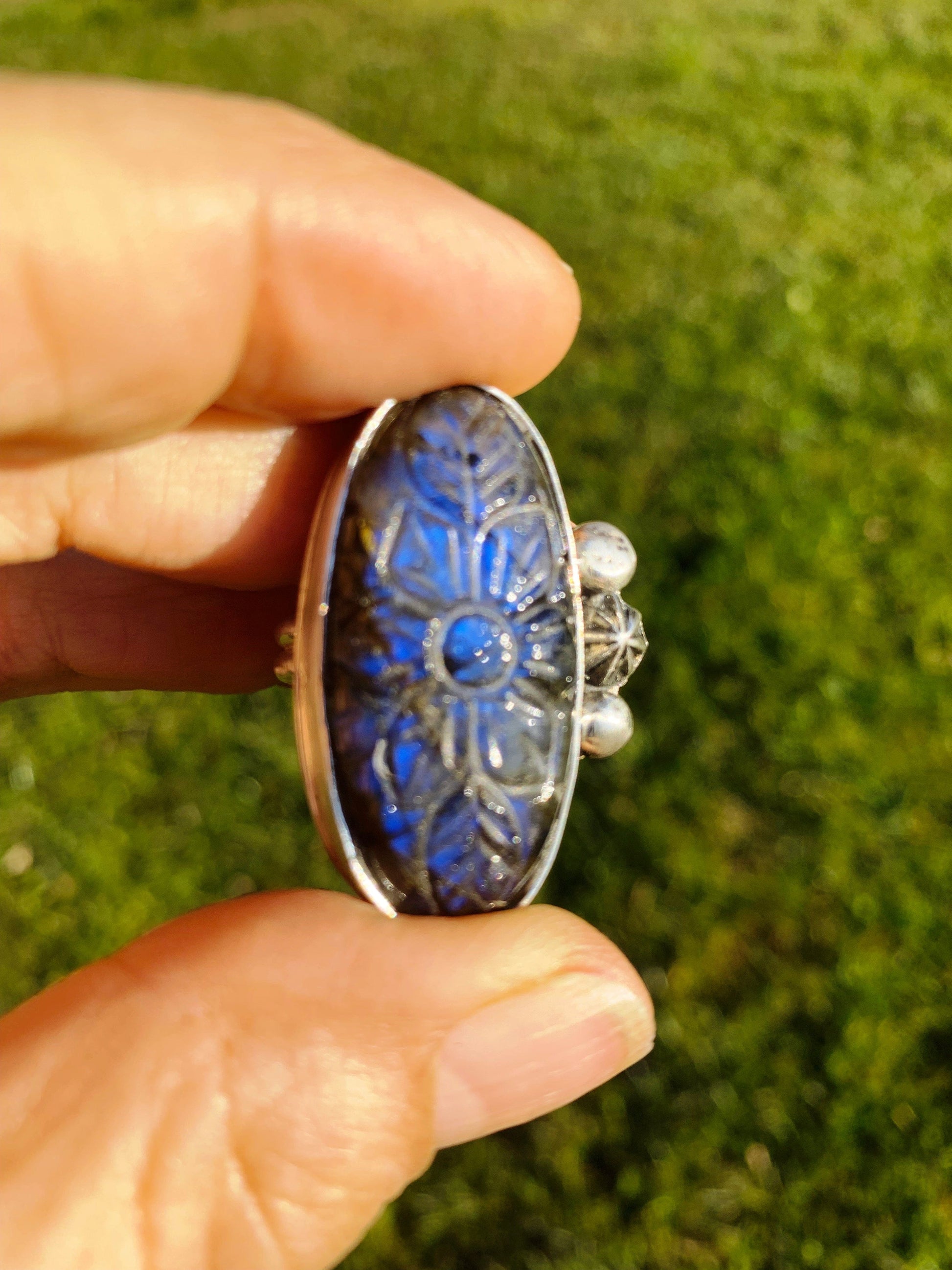 Carved labradorite ring held in hand, floral design.