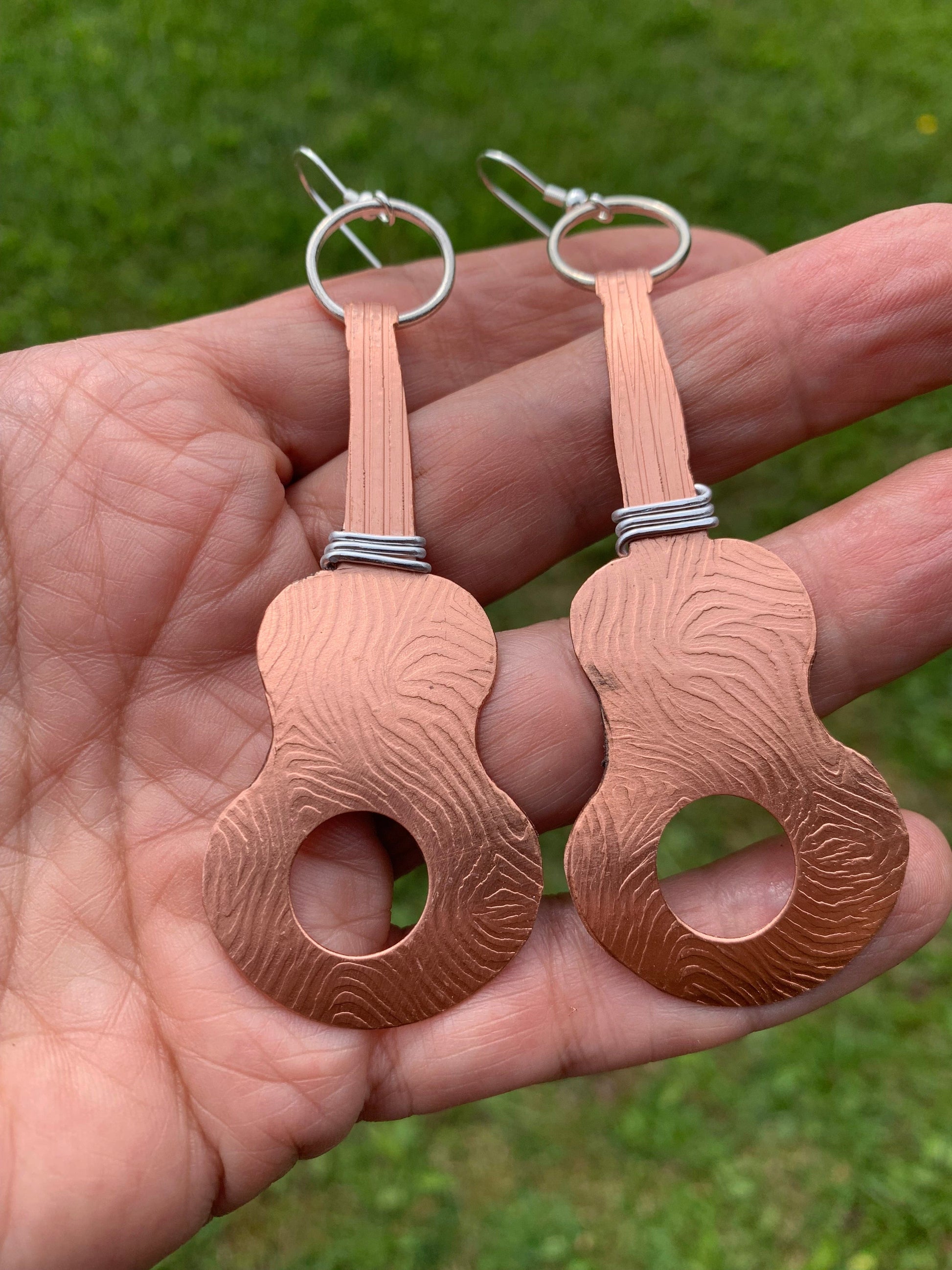 Guitar-shaped copper earrings held in hand