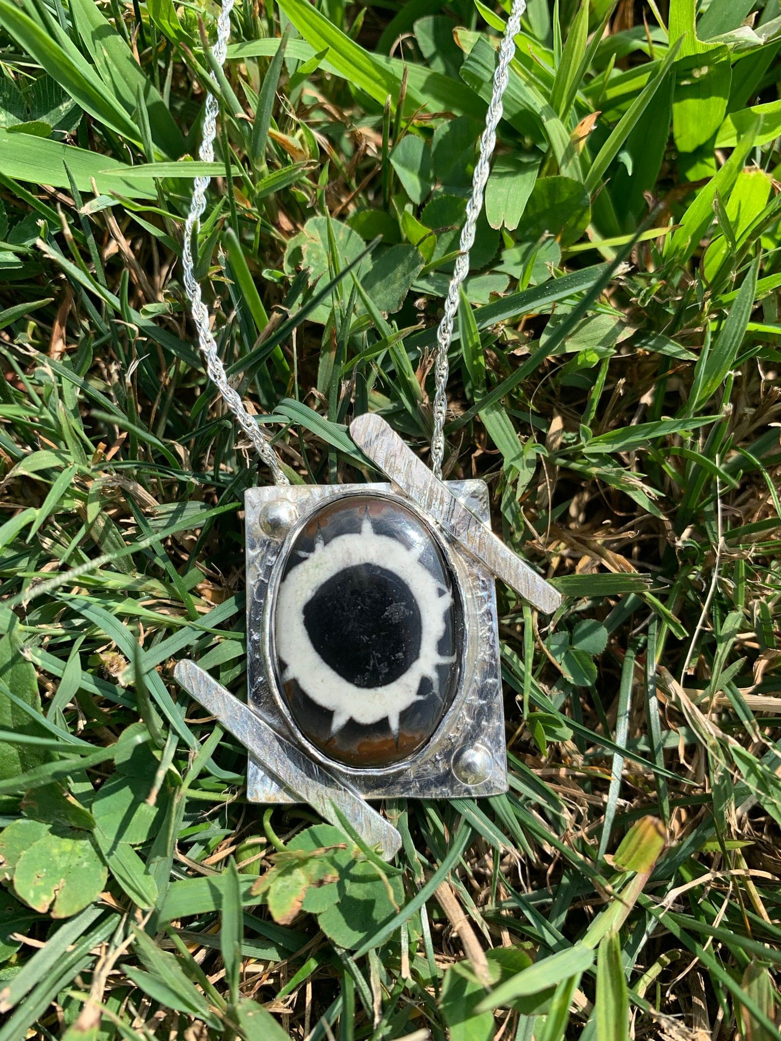 Necklace with black and white pendant on grass.