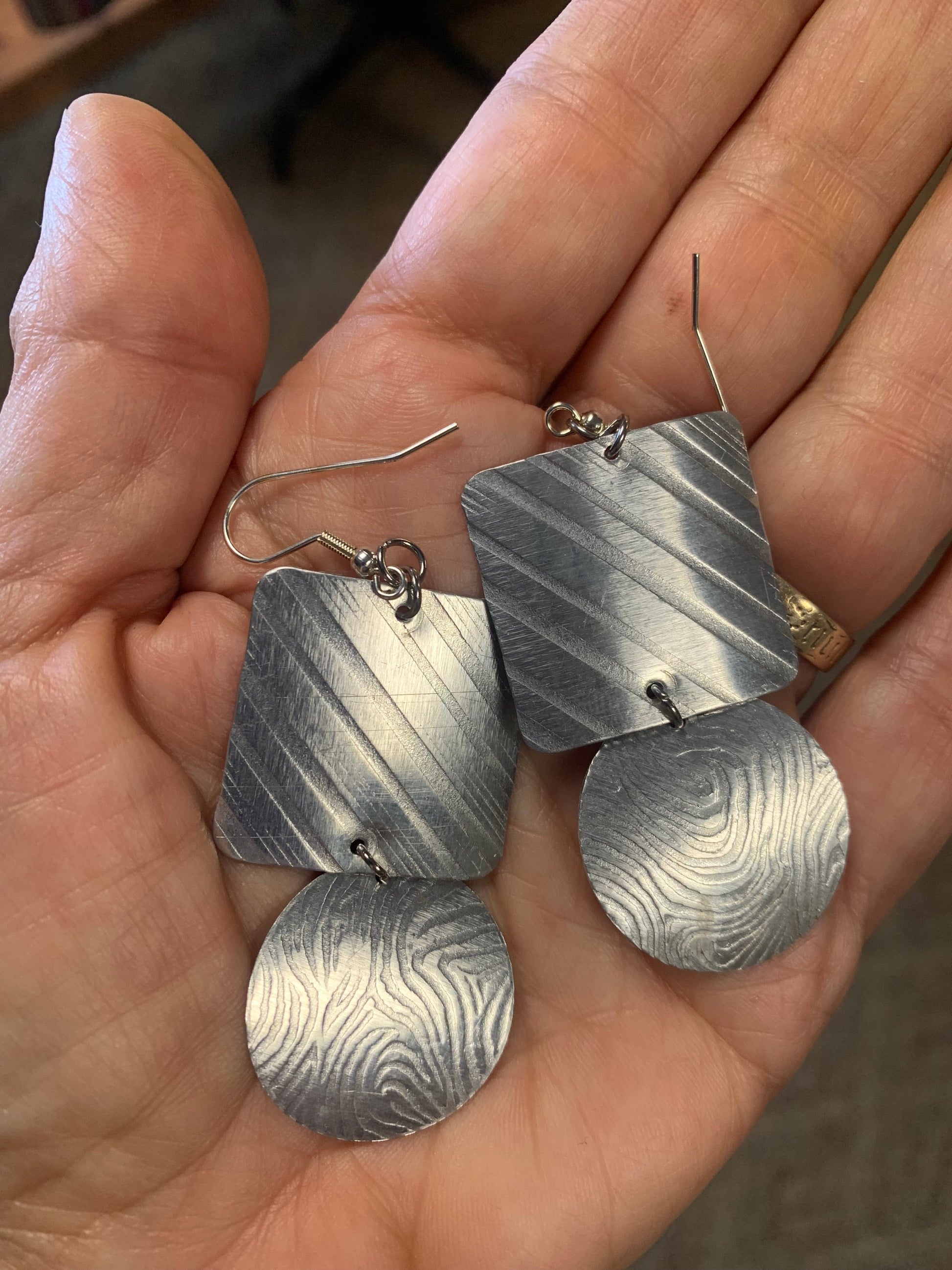 Silver earrings with lines and swirl patterns.