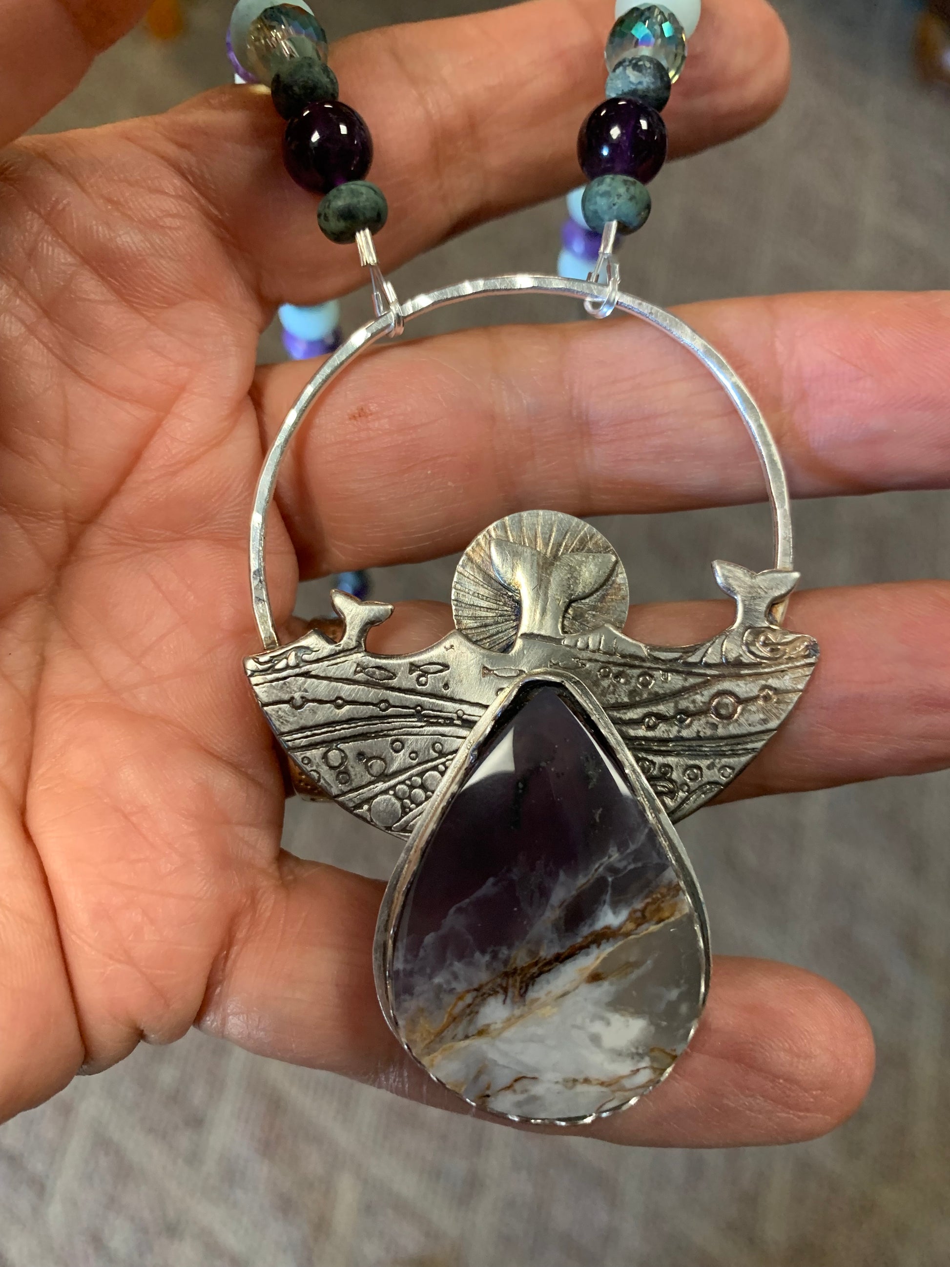 Silver pendant with a purple stone held in a hand