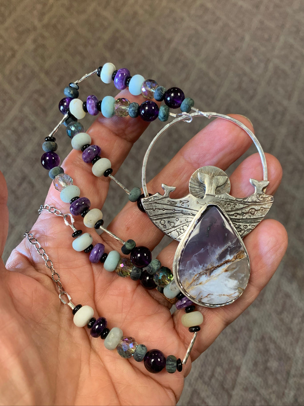 Hand holding a beaded pendant with a decorative clasp on a textured surface