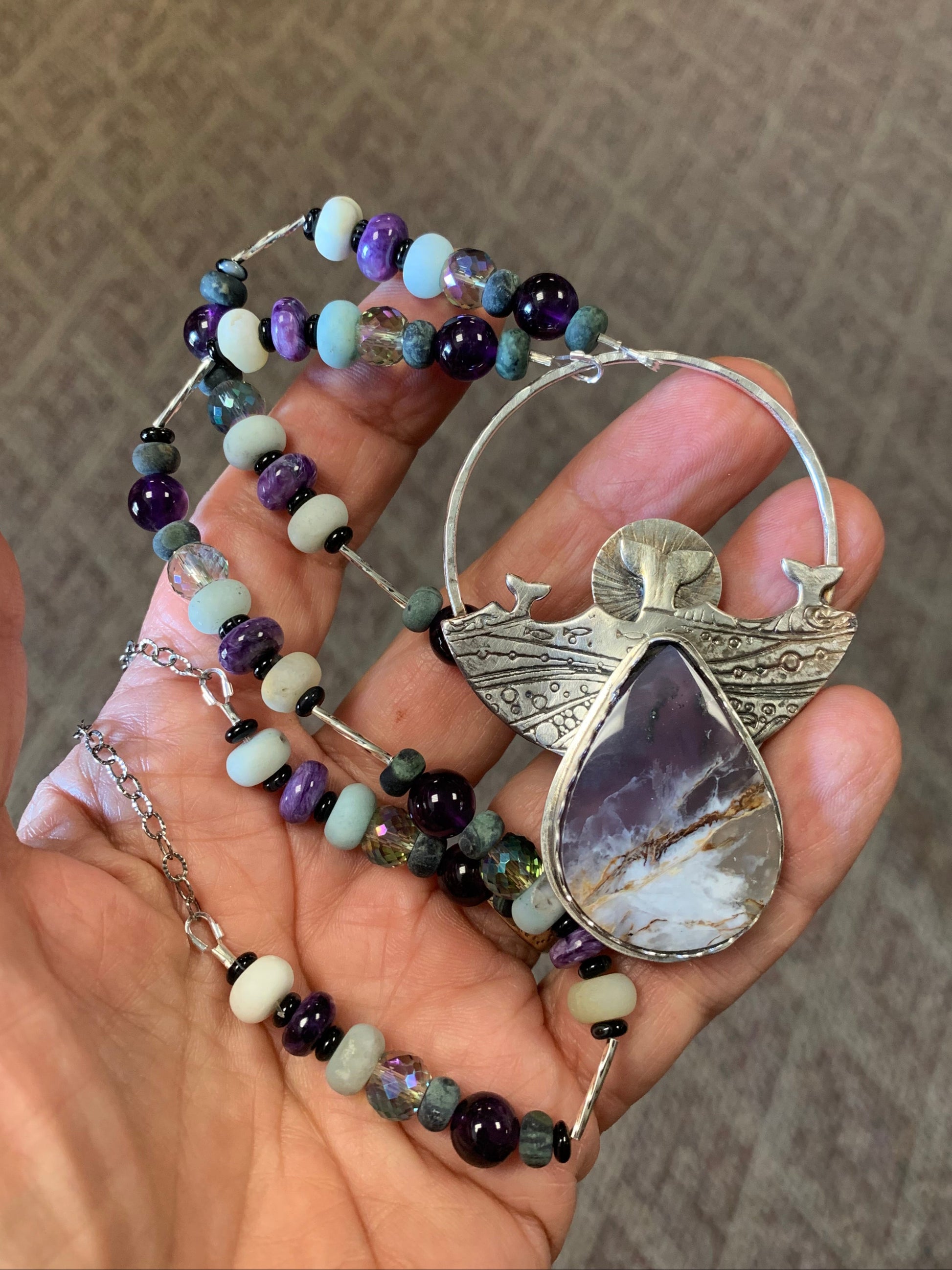 Hand holding a beaded pendant with a decorative clasp on a textured surface
