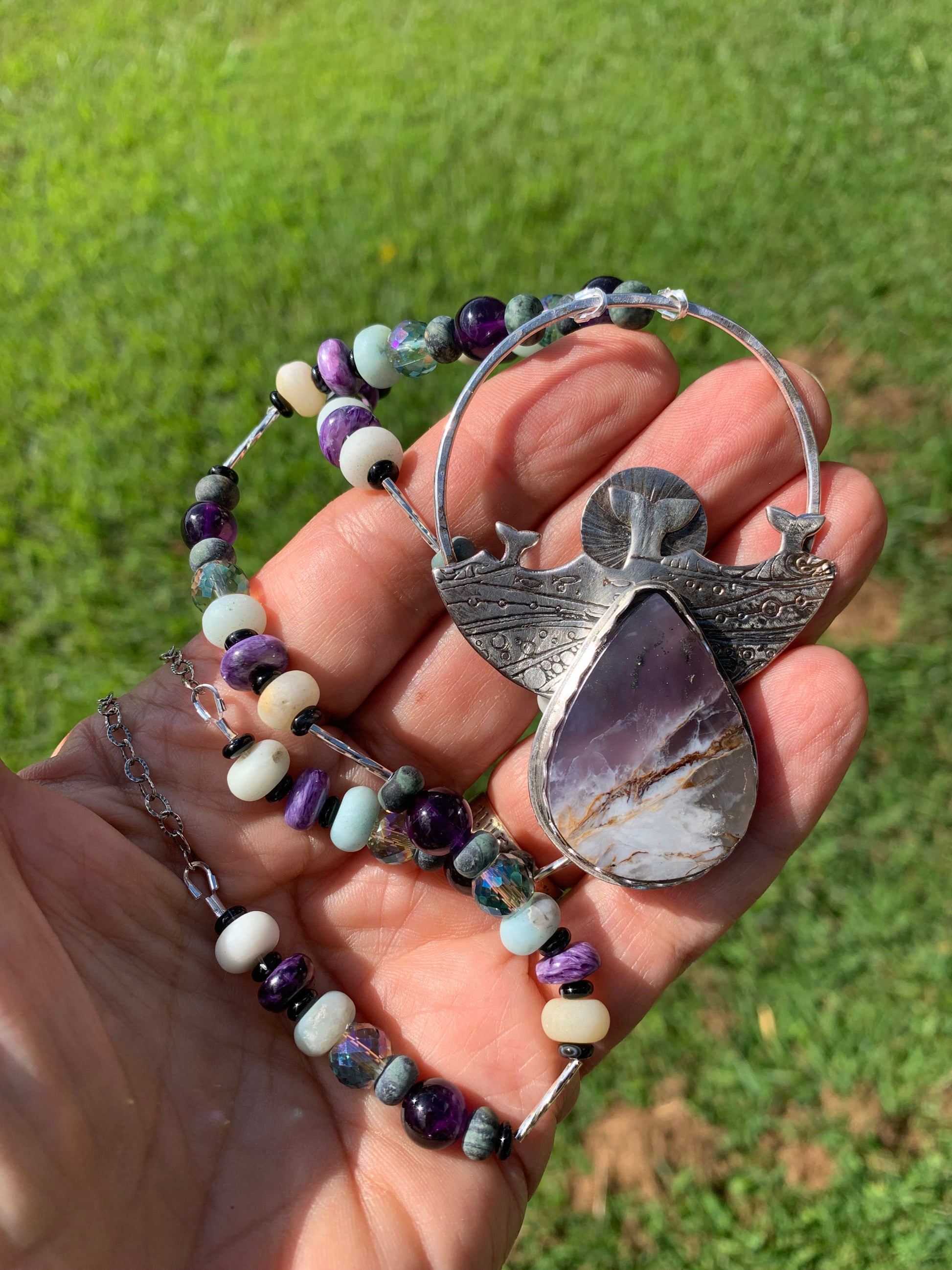 Hand holding a bracelet with a large Chalcedony stone against a grassy background