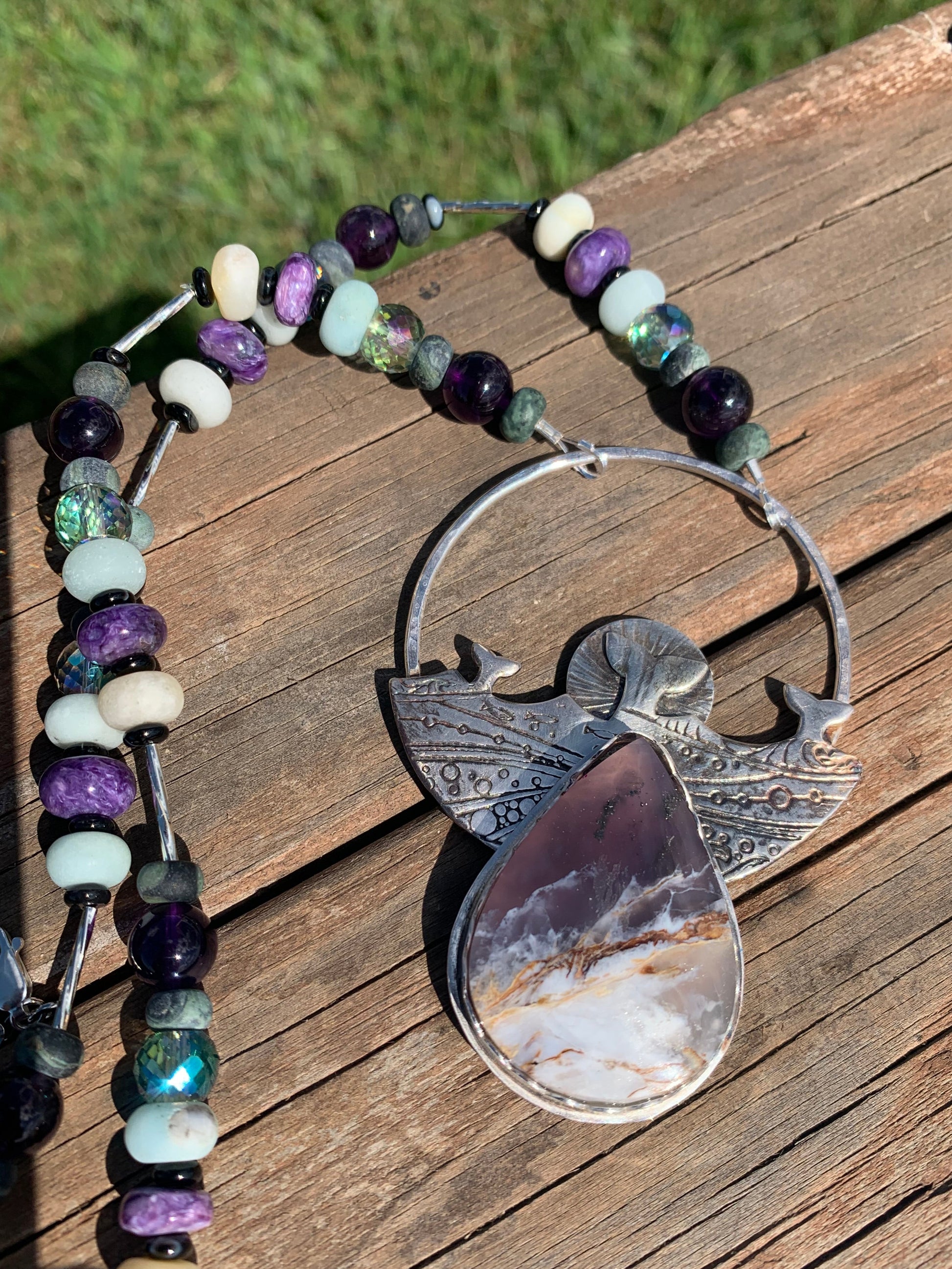 Necklace with beaded chain and large silver pendant on wooden surface