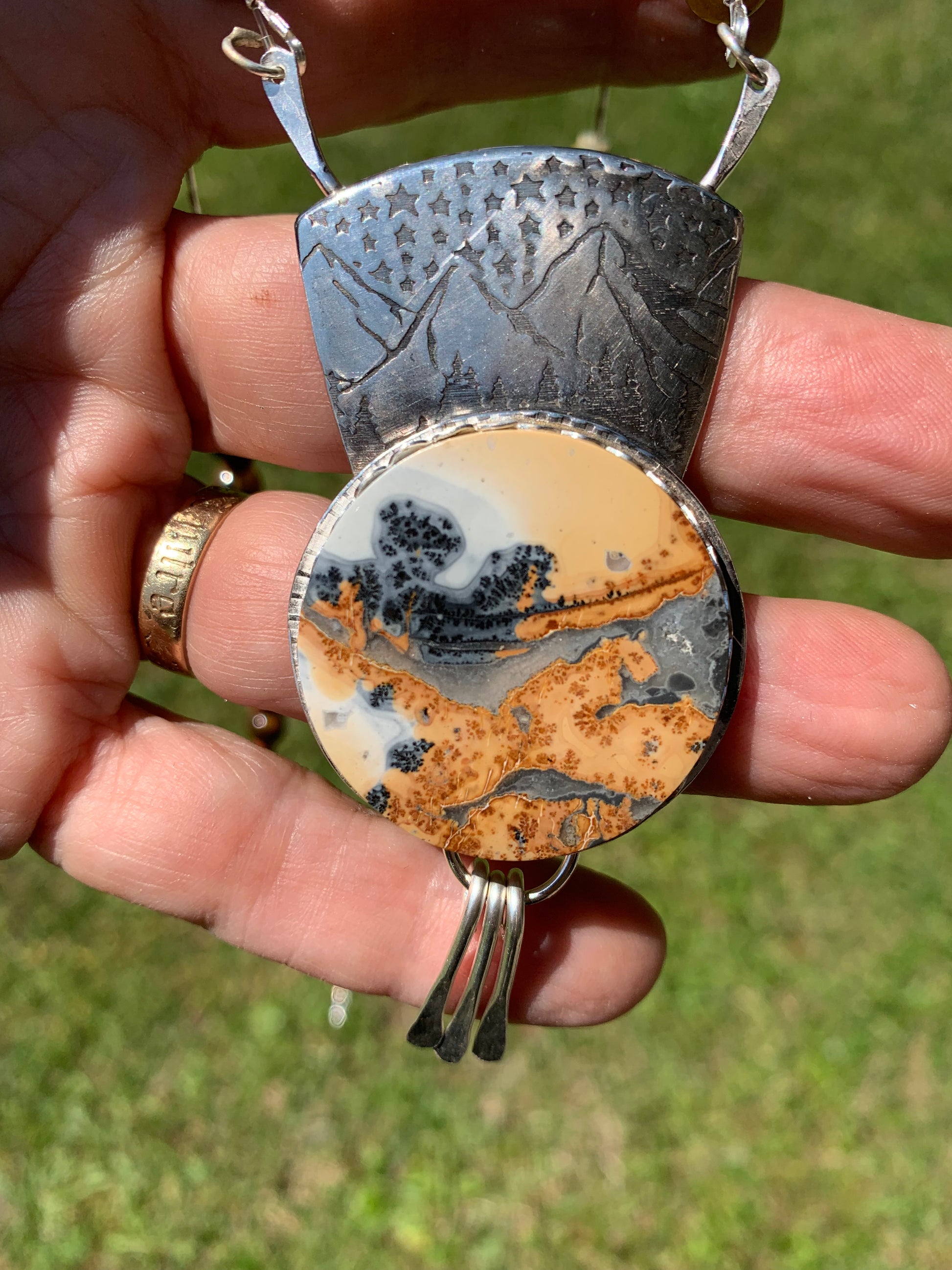 Hand holding a unique stone pendant with intricate patterns against a blurred green background
