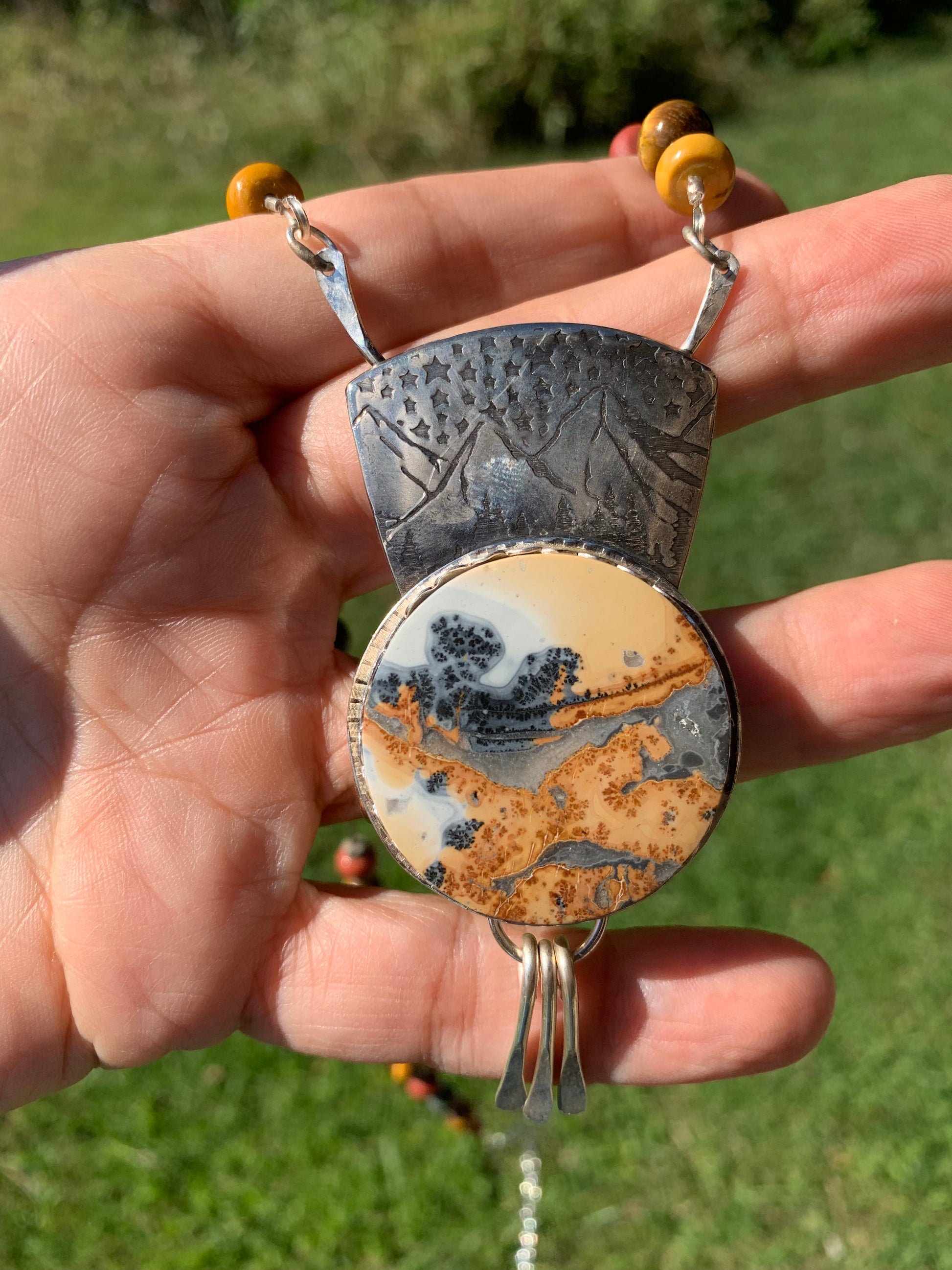 Hand holding a pendant with a natural stone design against a blurred green background