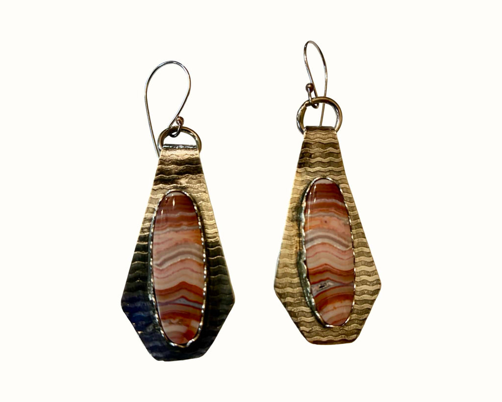 A pair of handmade teardrop-shaped dangle earrings featuring a polished band of orange and brown agate stone inlay, set in a hammered gold-tone metal frame with a silver-tone fishhook ear wire.