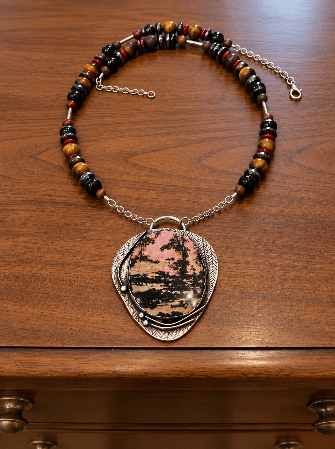 One-of-a-kind Rhodonite and sterling silver necklace with handmade earthy gemstone chain displayed on wood