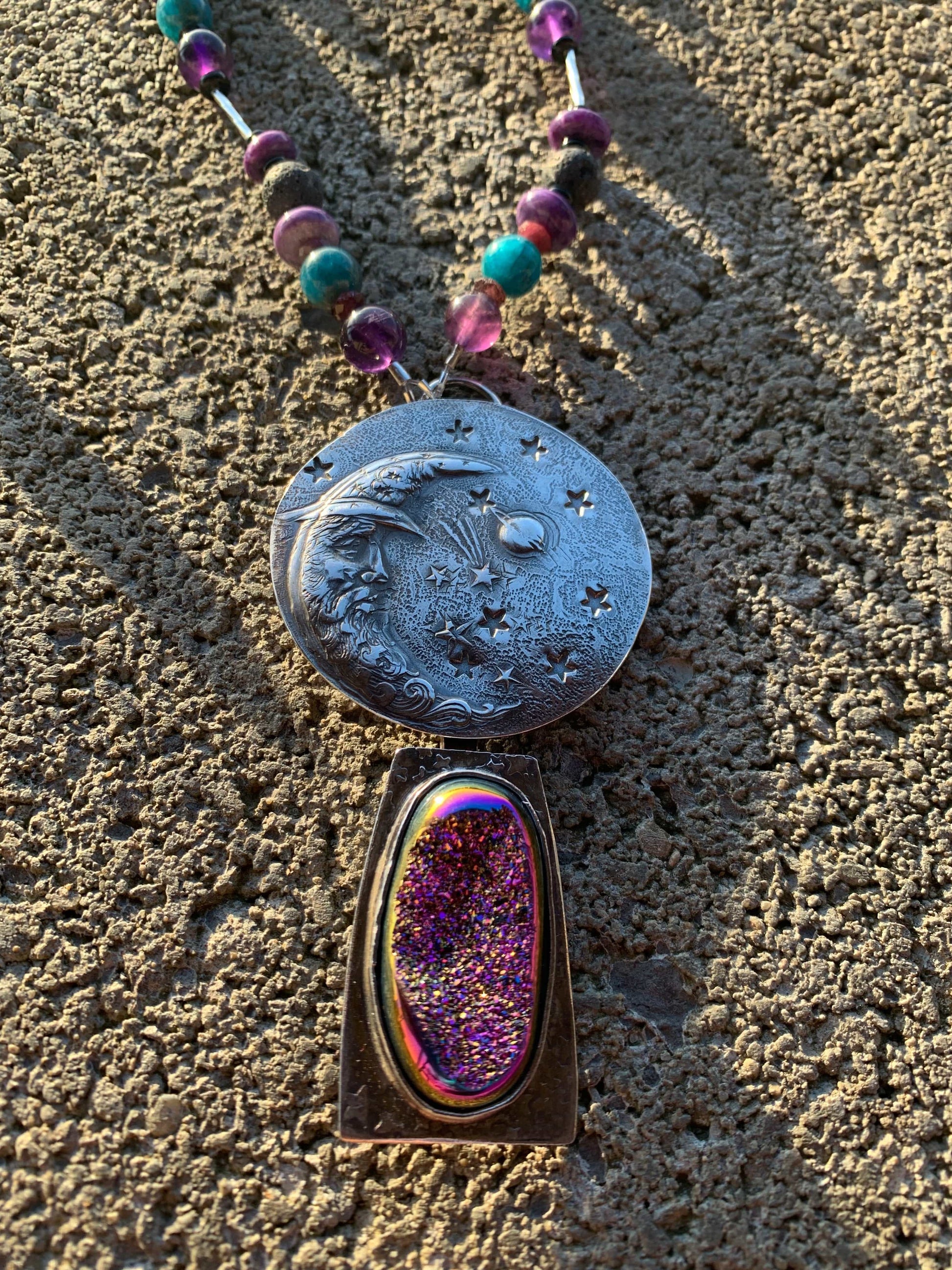 Decorative stone with engraved design and colorful bead necklace on textured surface