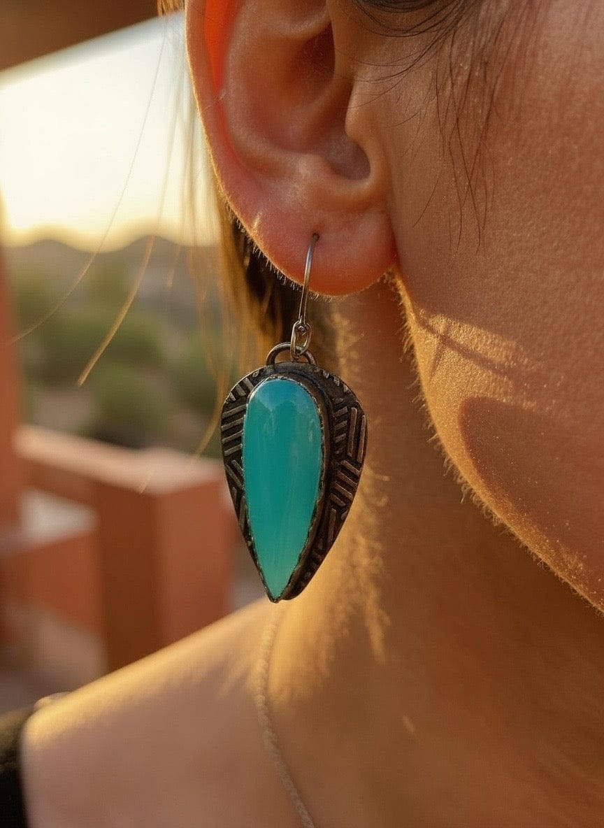 Close-up of a turquoise earring worn by a person with a blurred outdoor background