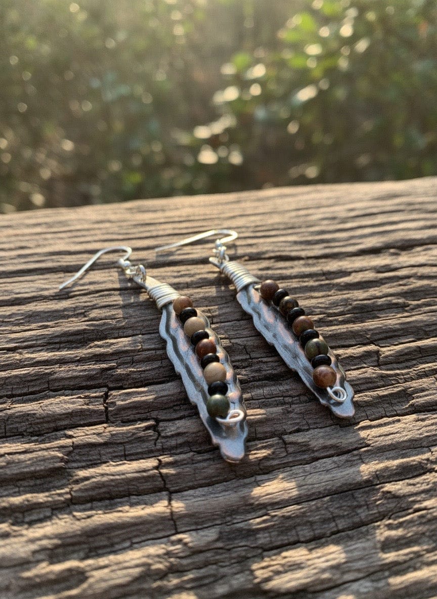Pair of beaded feather earrings on a wooden surface with a blurred natural background