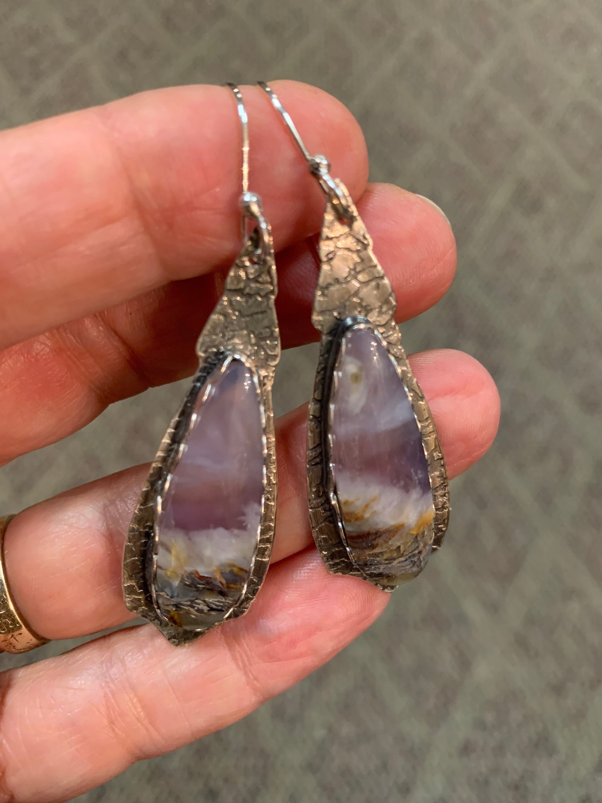 Hand holding two silver earrings with purple stone accents with captured beach scene against a neutral background 