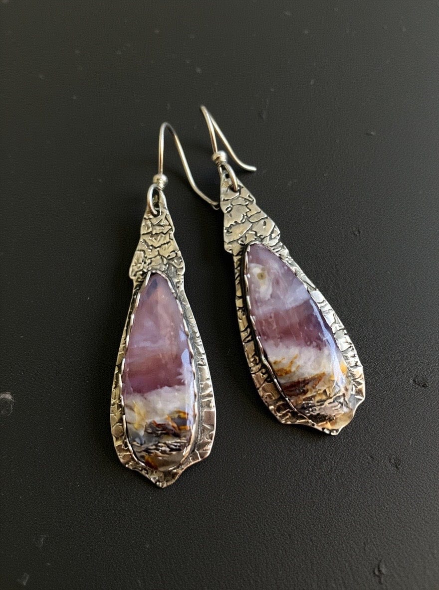 Teardrop-shaped earrings with textured silver frames on a black background