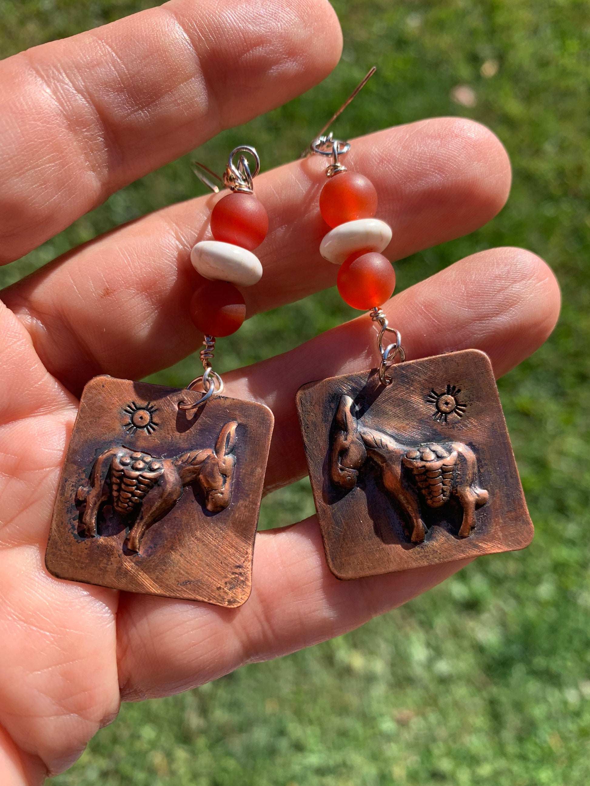 Copper earrings with animal designs held in a hand against a grassy background