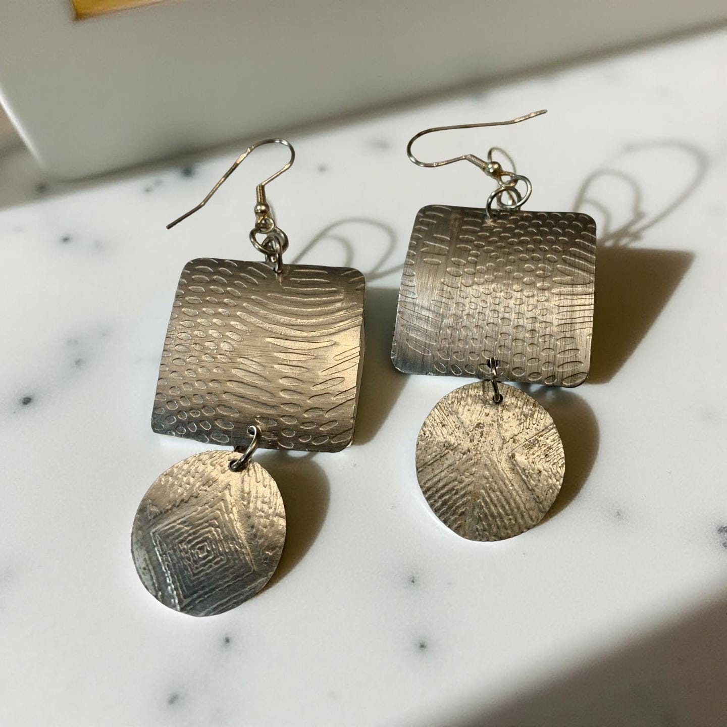 Pair of silver textured aluminum earrings on a marble surface