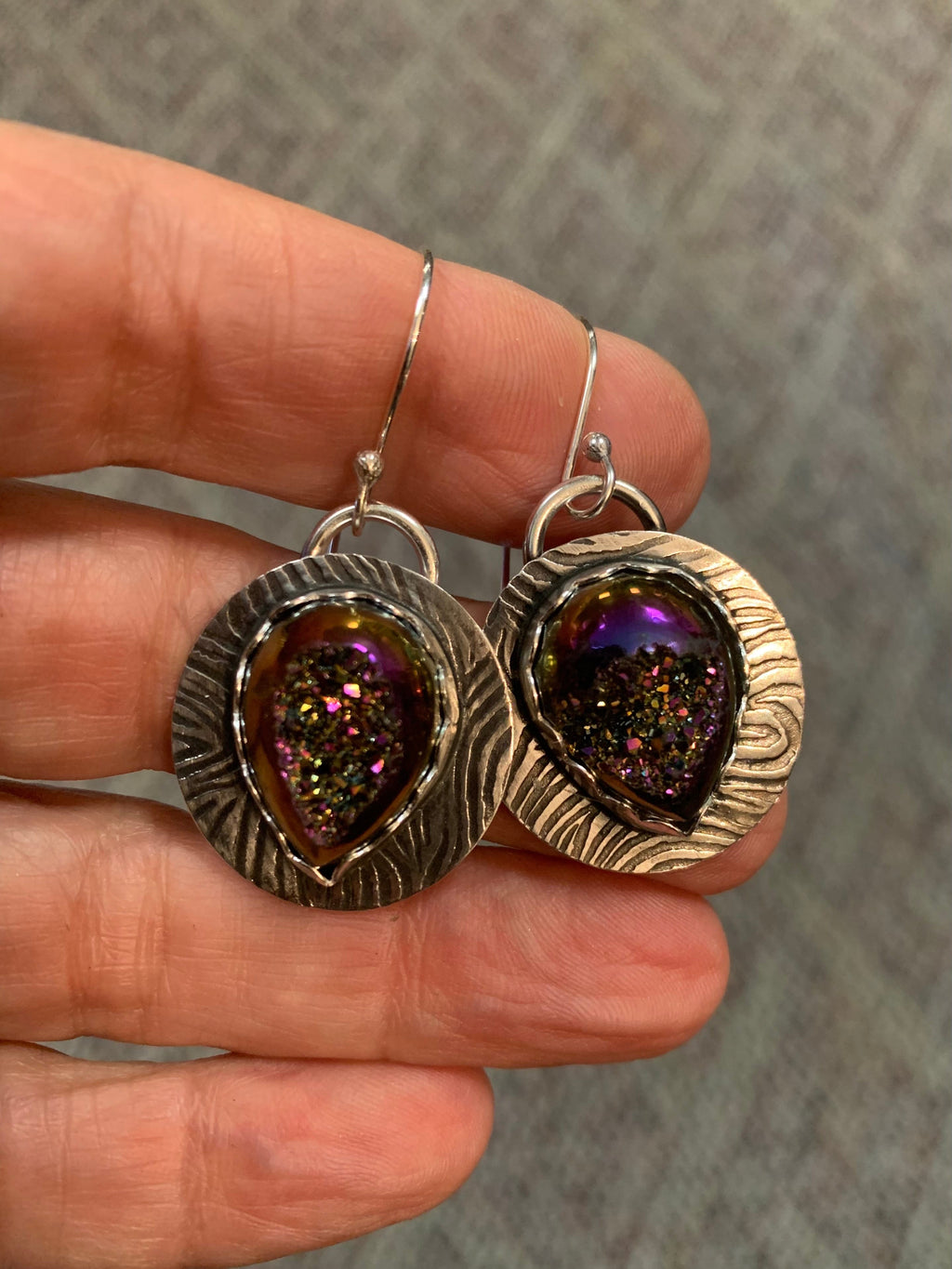 Silver earrings with purple gemstones held between fingers against a neutral background