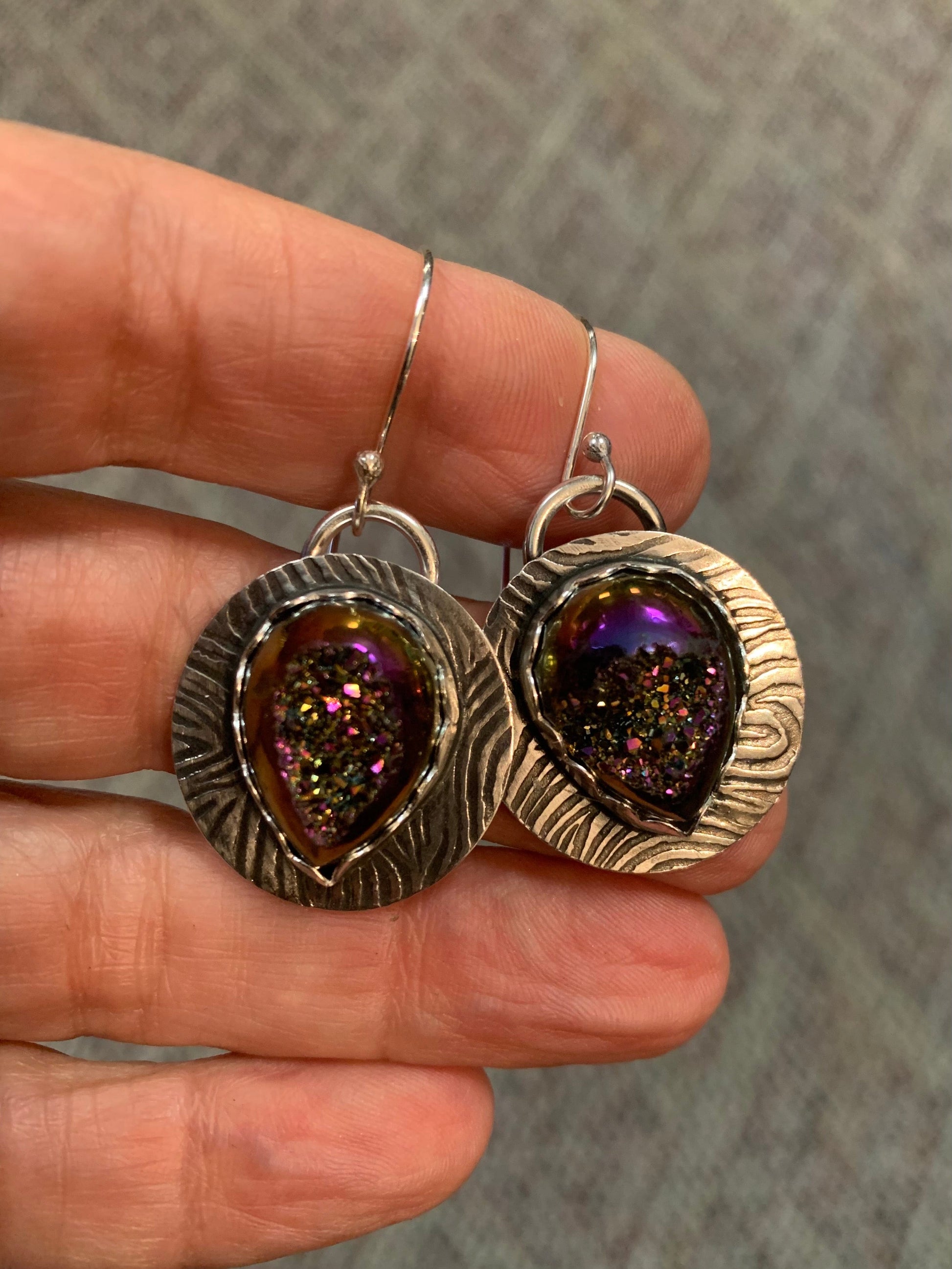 Silver earrings with purple gemstones held between fingers against a neutral background