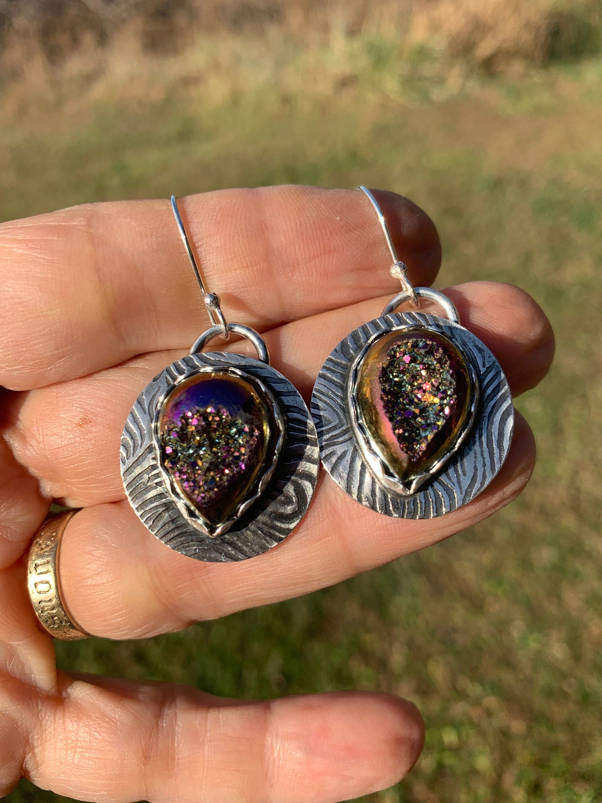  Silver earings with eye-shaped designs held by a hand against a blurred natural background.