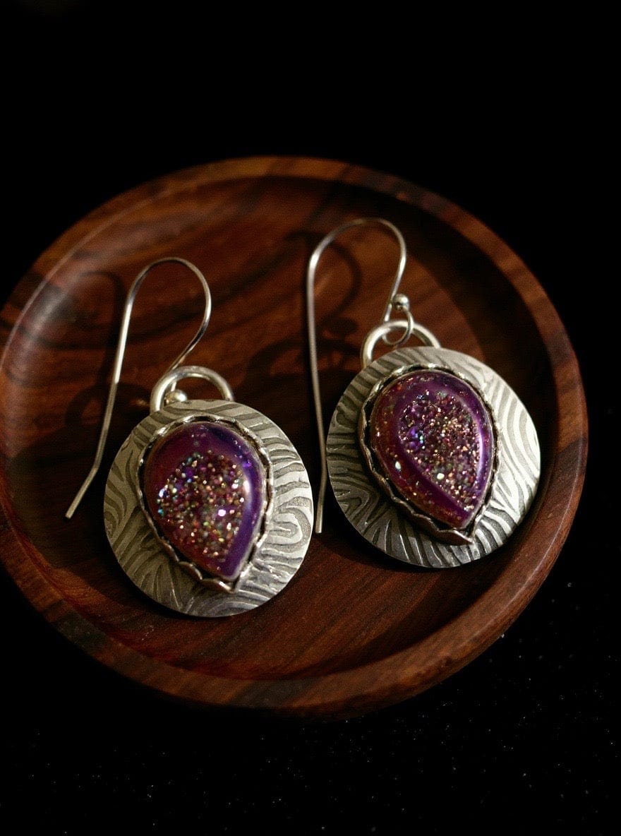 Silver earrings with purple and pink speckled stones on a wooden surface
