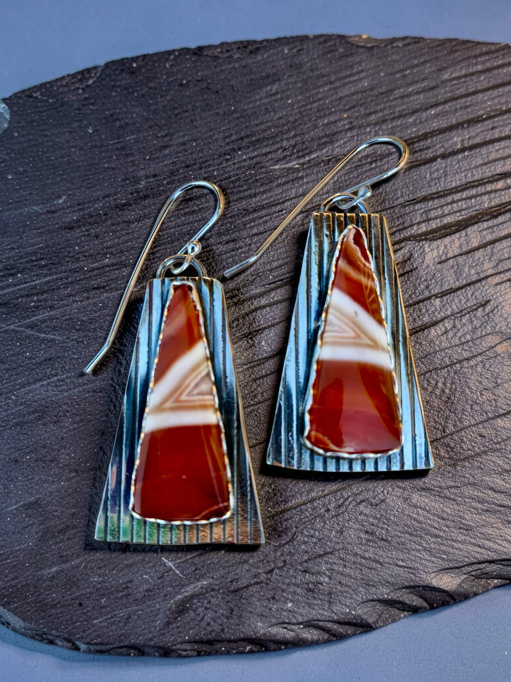 One-of-a-kind Echoes in the Stone earrings by Christine Keller, featuring red and cream banded agate gemstones set on elongated textured silver backplates with silver ear wires.