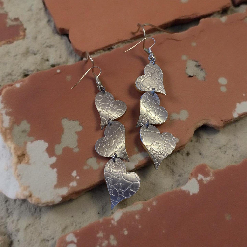 Silver heart-shaped aluminum earrings on a textured stone surface