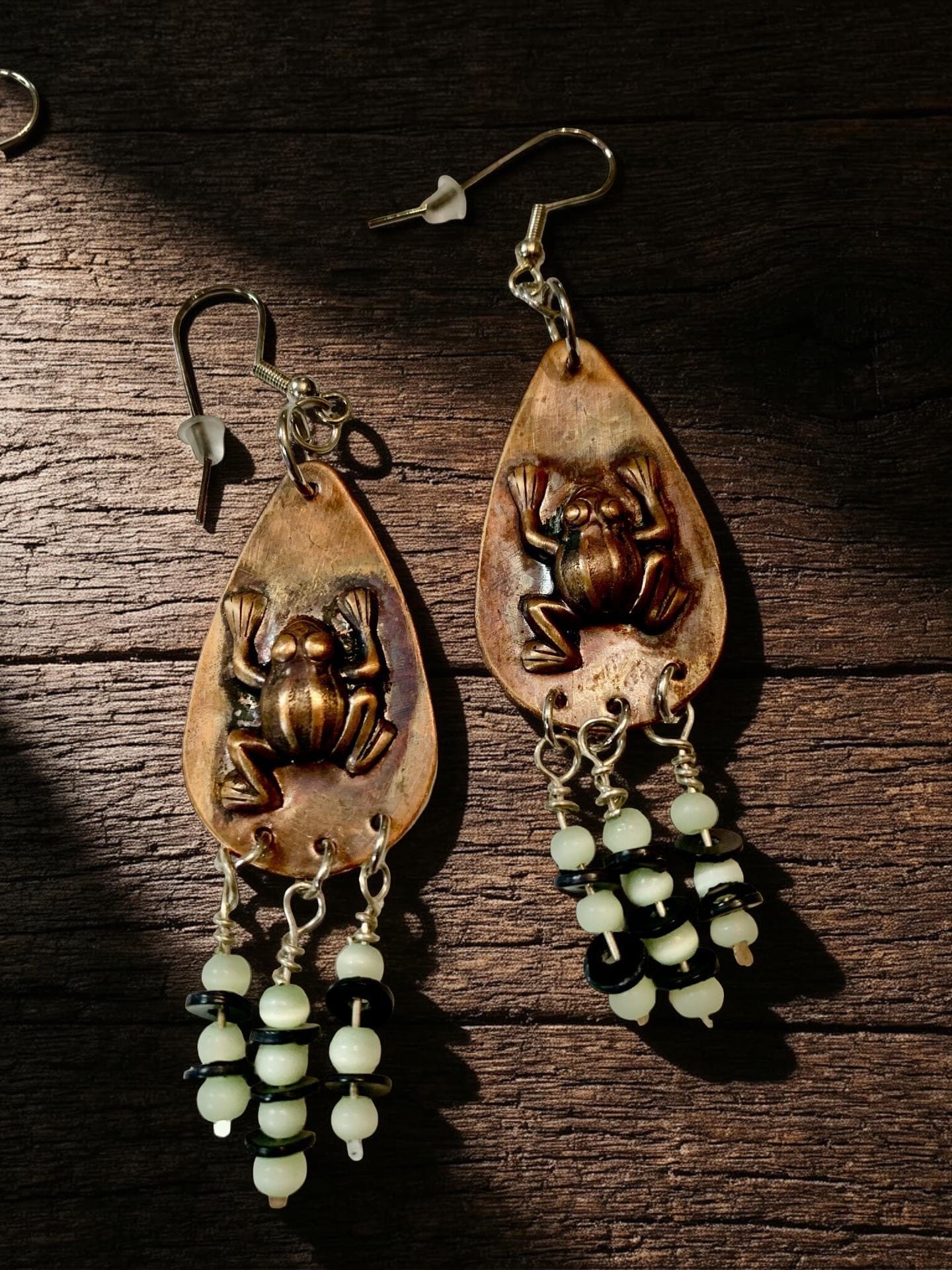 Pair of Copper-colored earrings with frog designs on a wooden surface