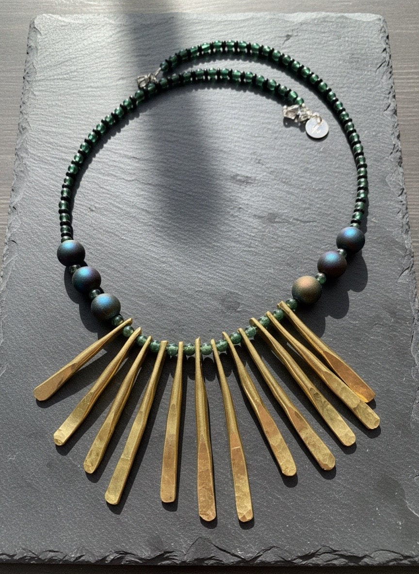 Necklace with green beads and brass fringe on a gray stone surface