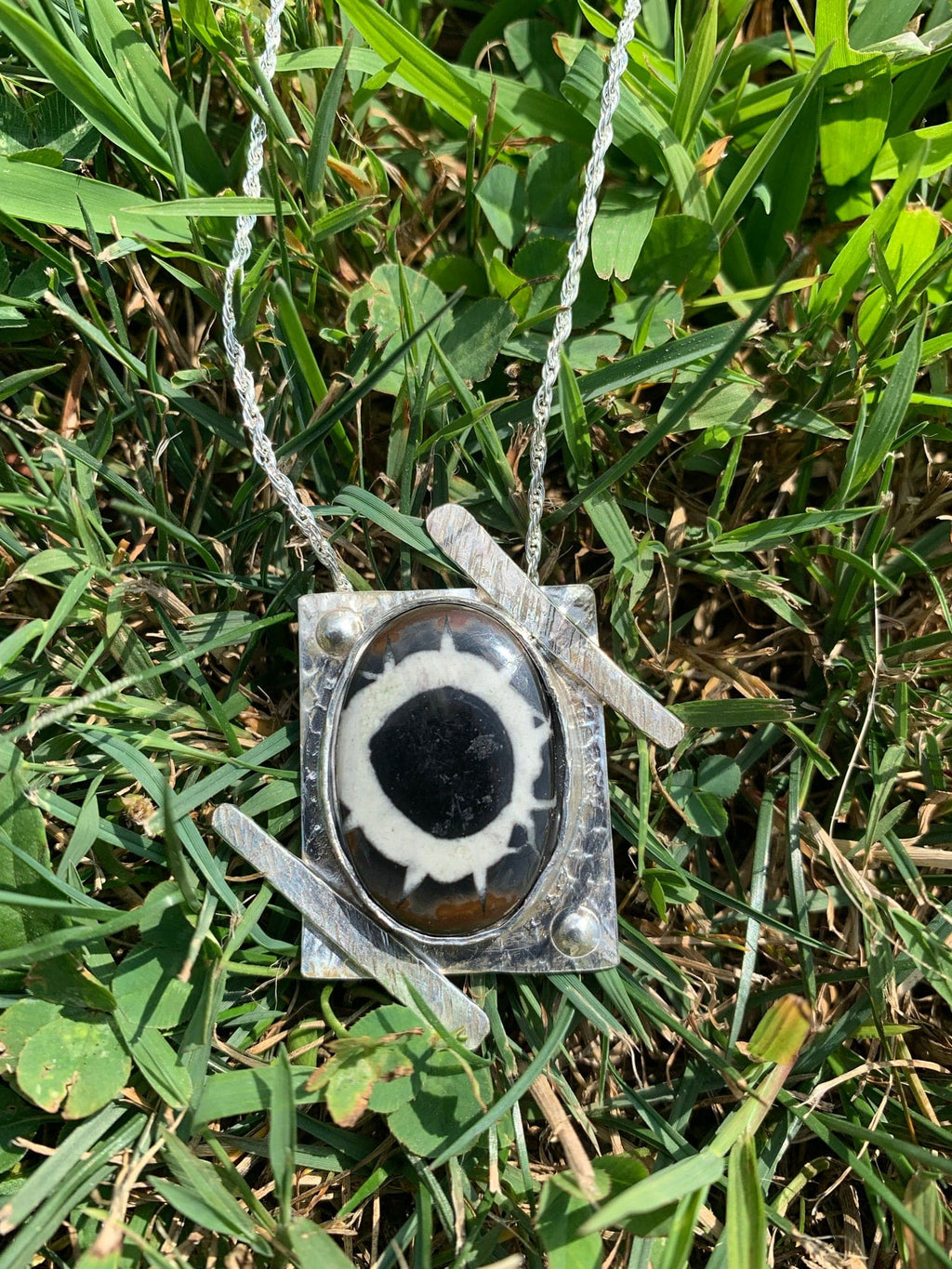 Necklace with black and white pendant on grass.