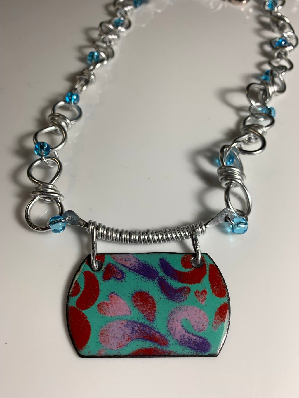 Necklace with turquoise pendant, red and purple design, silver chain.