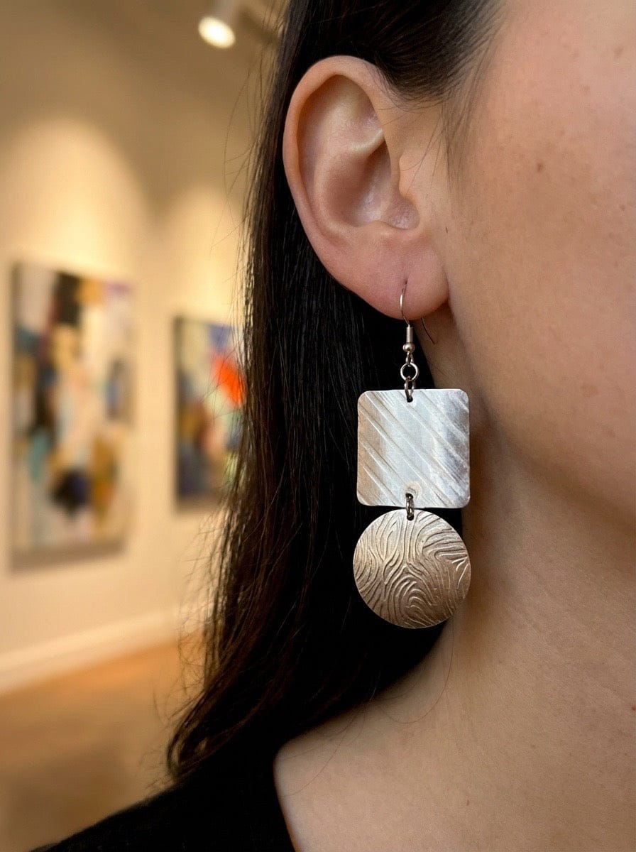 Close-up of a person wearing a silver earring with a textured design in an indoor setting.