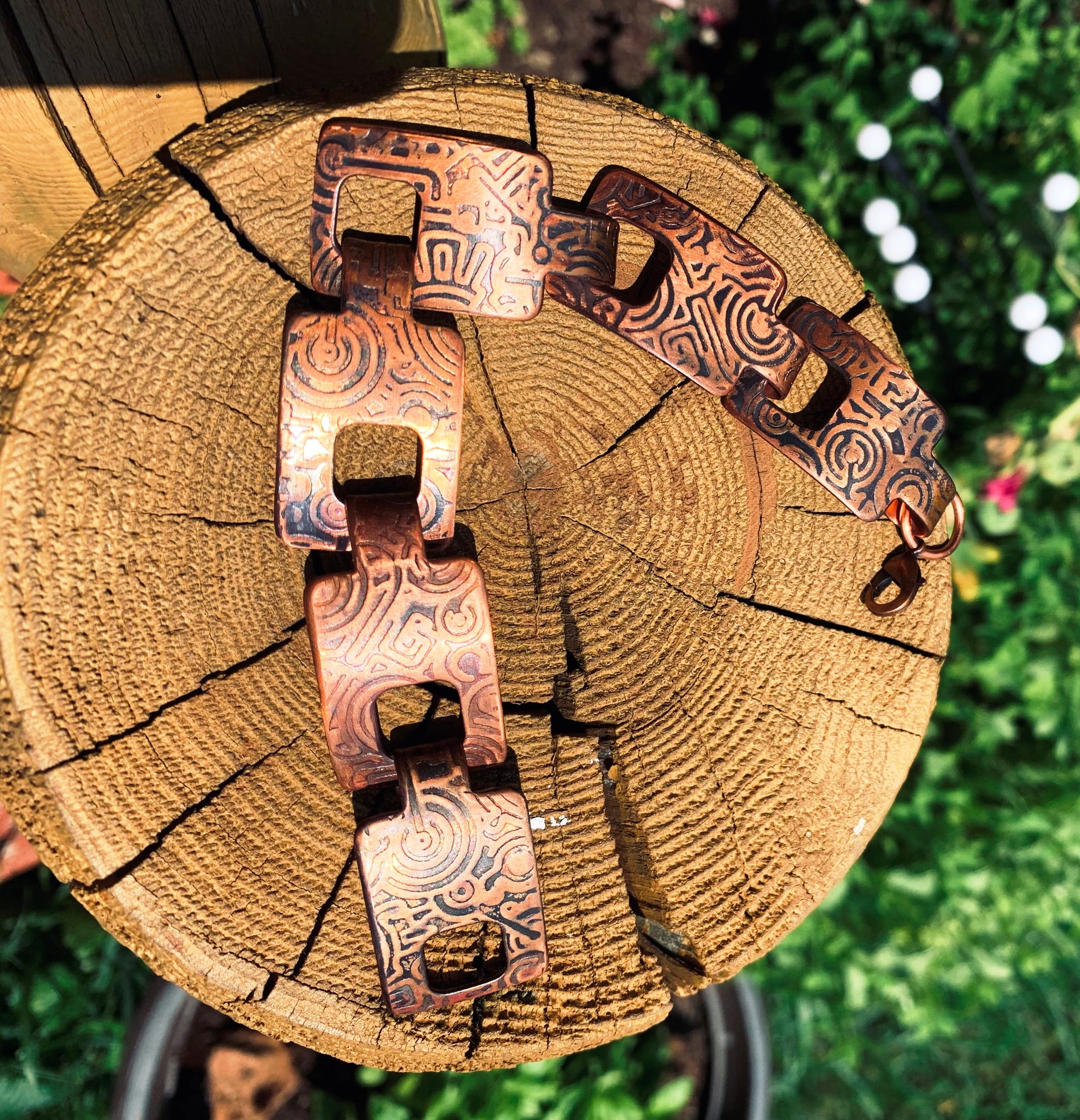 Decorative copper bracelet on a wooden log with blurred greenery in the background