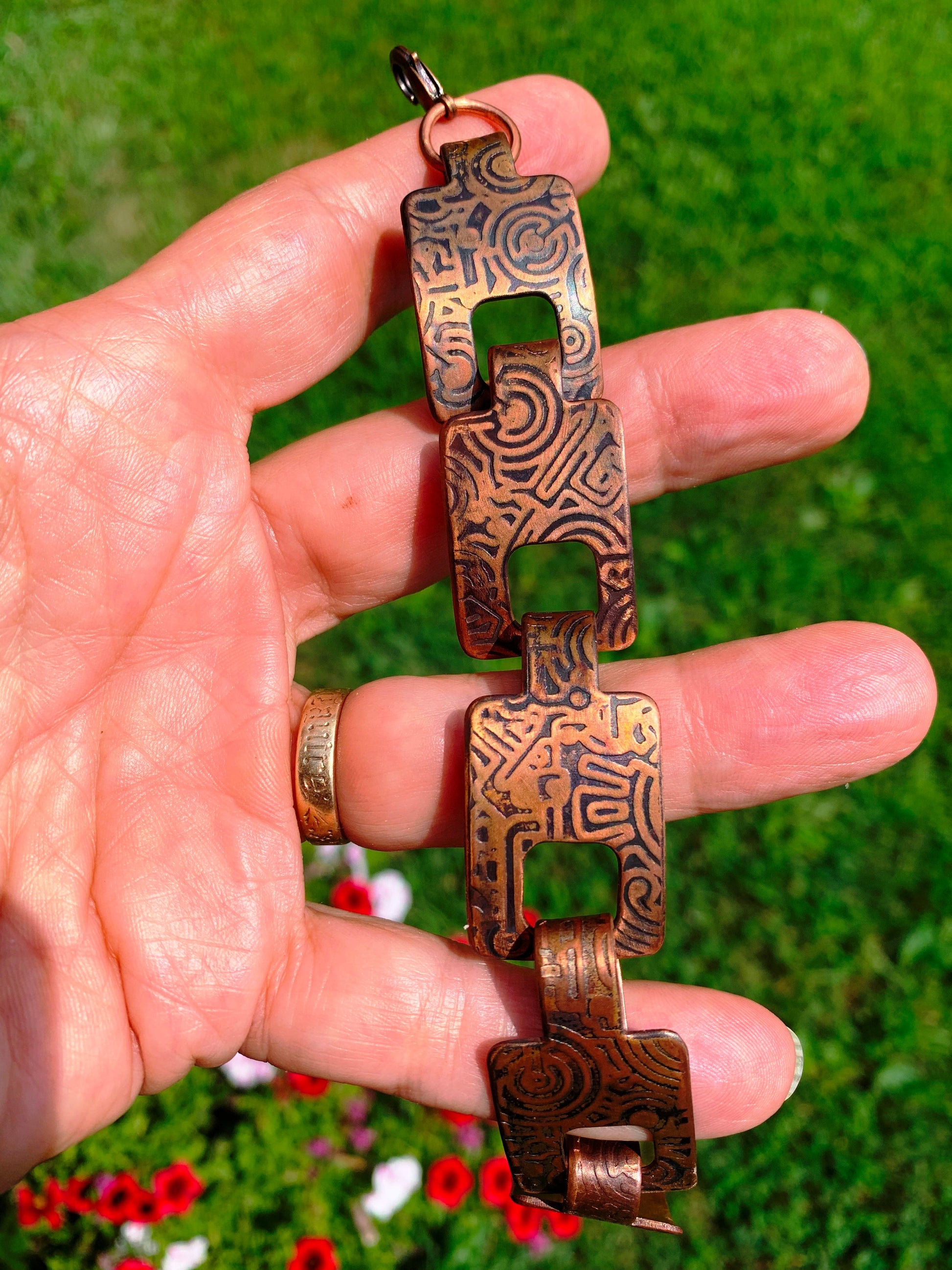 Hand holding a copper bracelet with intricate designs against a green grass background