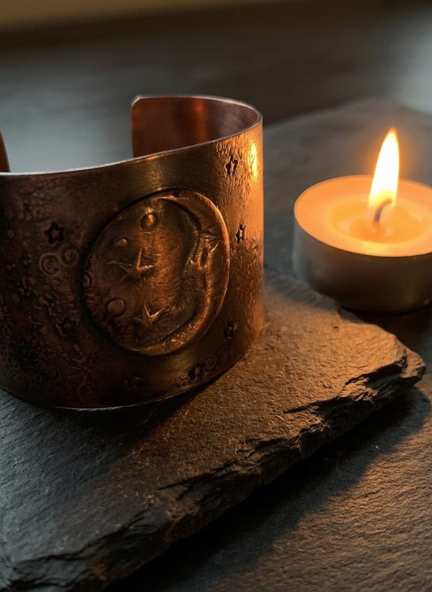 Copper bracelet with embossed design on a dark surface next to a lit candle