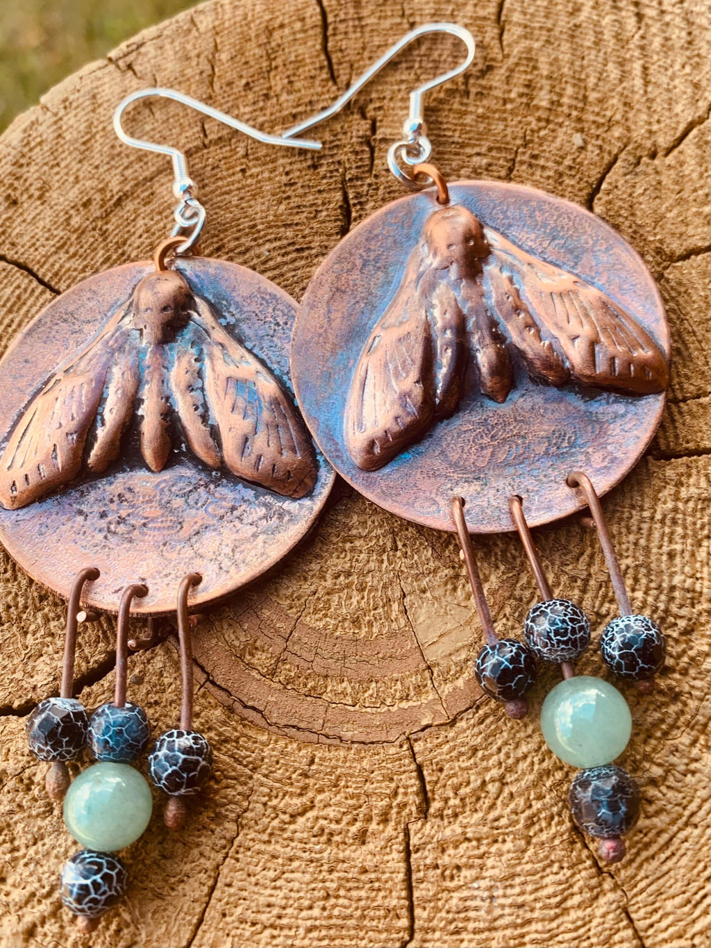 Copper moth earrings with bead accents on a wooden surface