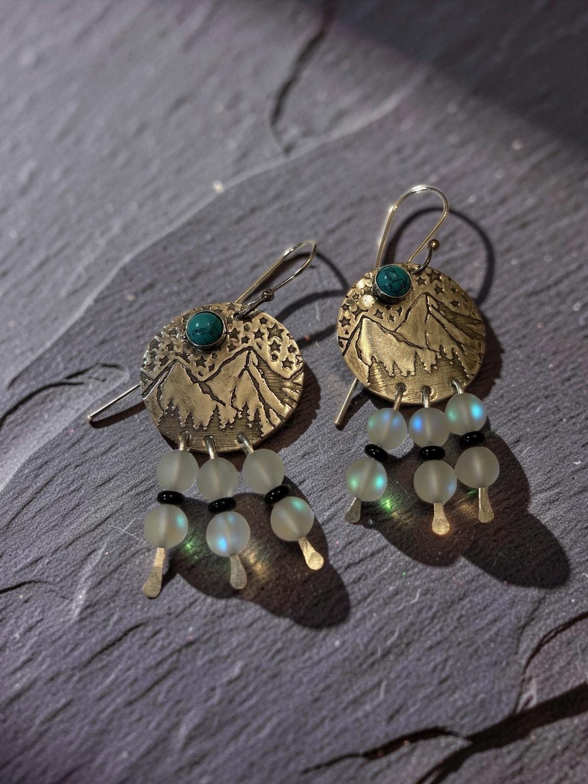 Mountain View handcrafted brass earrings featuring engraved mountain landscapes with genuine turquoise, aurora glass bead dangles, black onyx accents, and sterling silver ear wires.