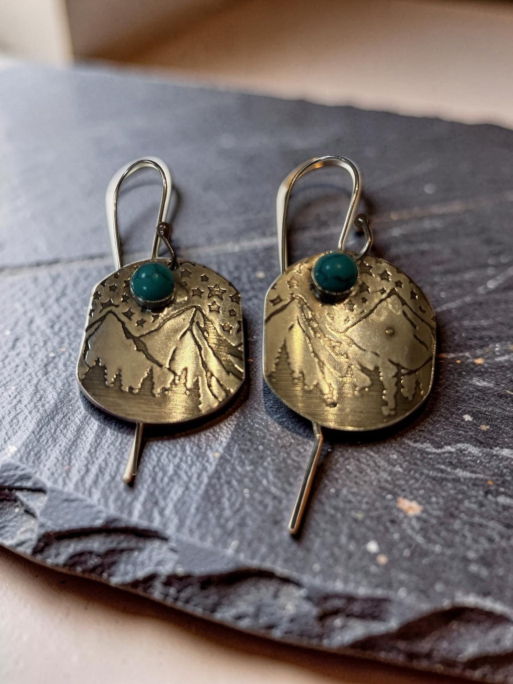 Handcrafted sterling silver Mountain Majesty earrings featuring engraved mountain landscapes beneath a star-filled sky with genuine turquoise cabochons.