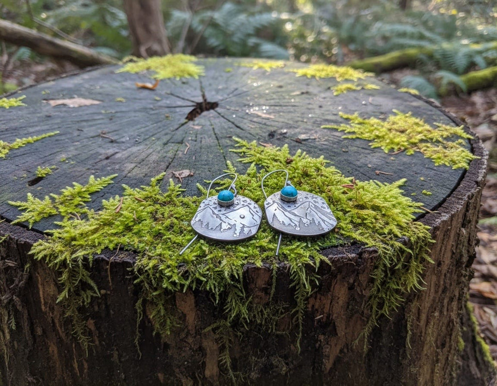 Handcrafted sterling silver Mountain Majesty earrings featuring engraved mountain landscapes beneath a star-filled sky with genuine turquoise cabochons.