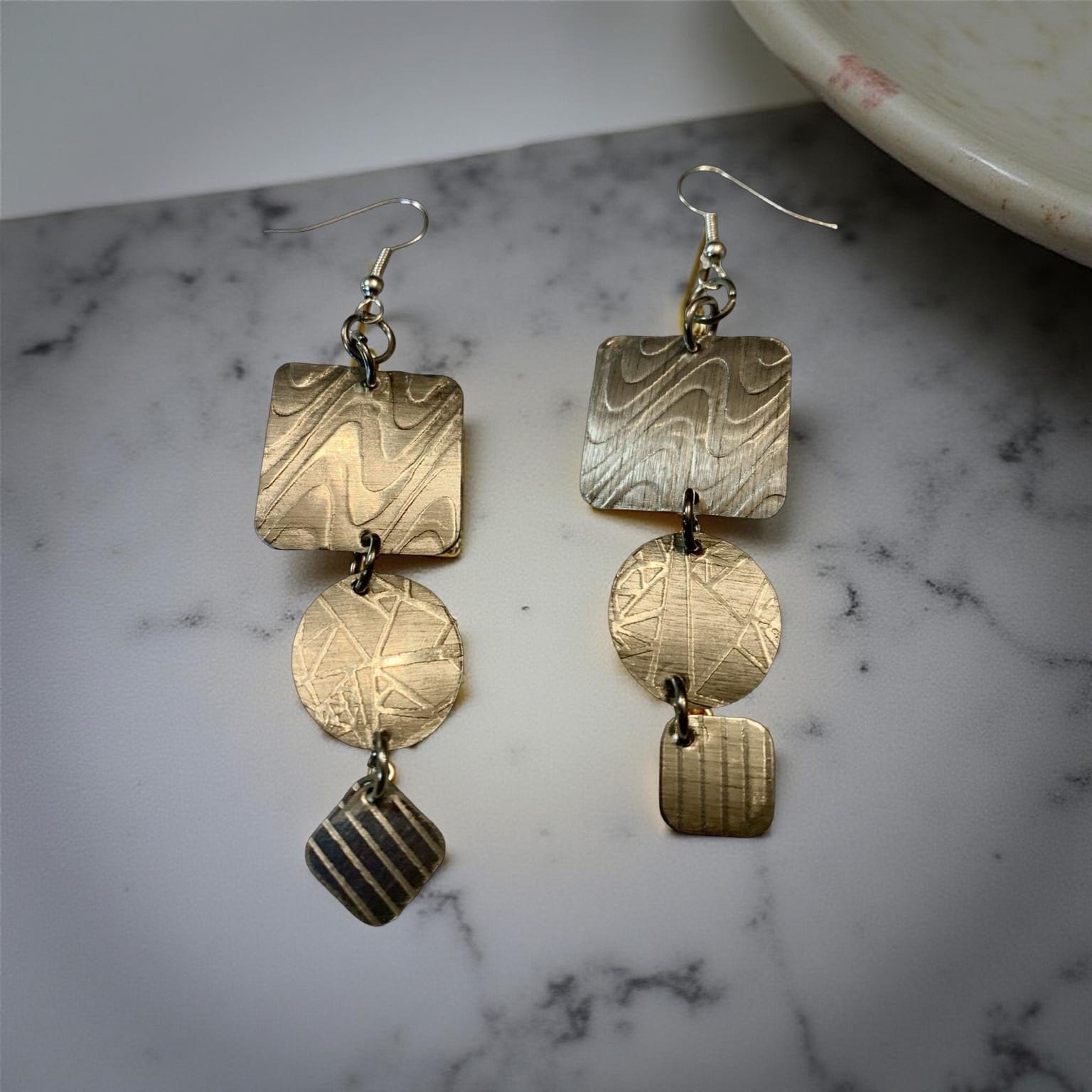 Aluminum earrings with geometric designs on a marble surface