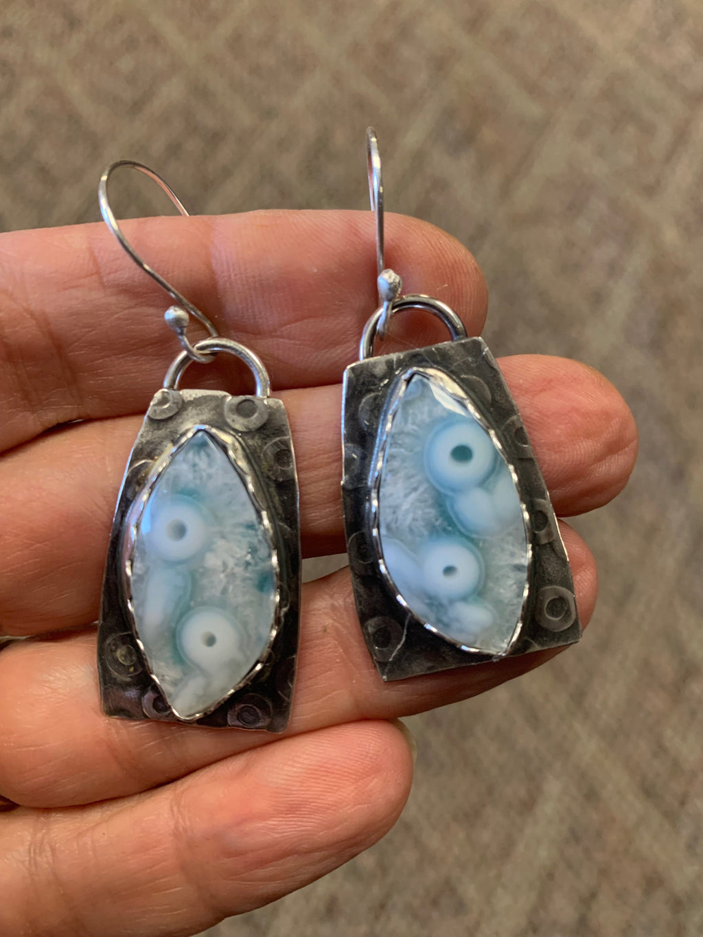 Silver earrings with eye-shaped stones held in a hand against a textured background