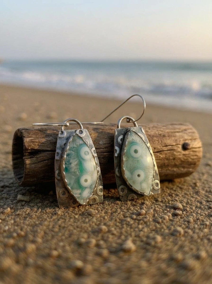 Pair of earrings on a piece of driftwood with a beach background