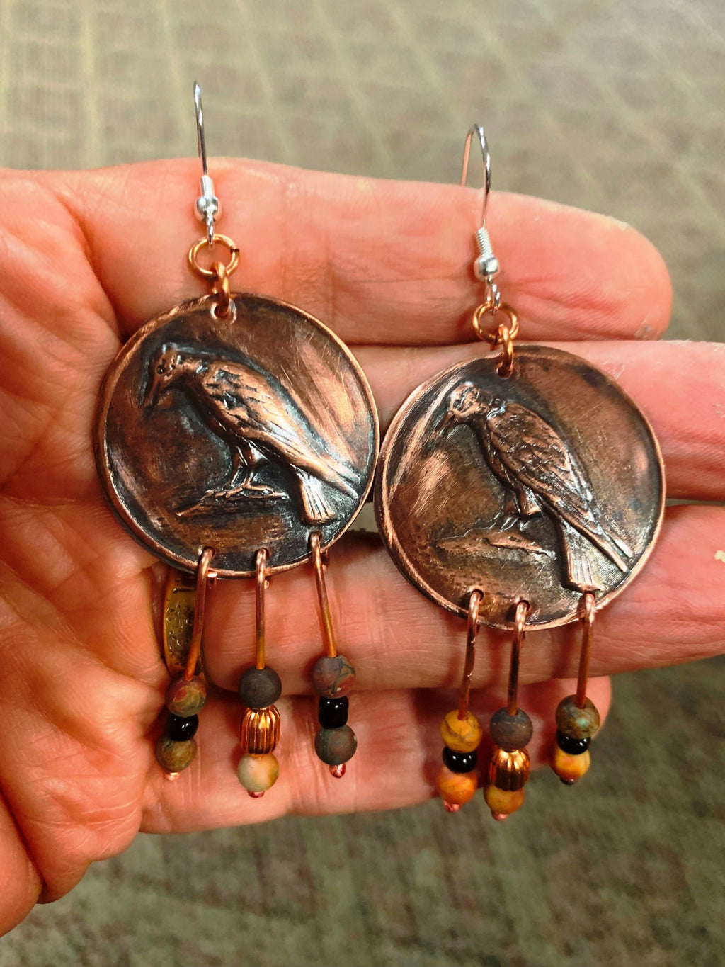 Copper coin earrings with bird designs held in a hand against a neutral background