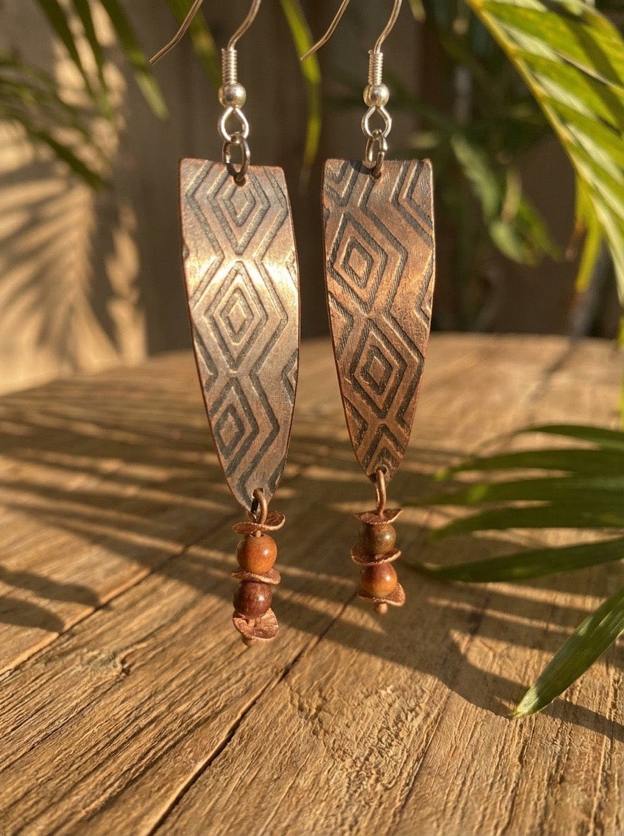 Pair of tribal-style earrings on a wooden surface with green leaves in the background