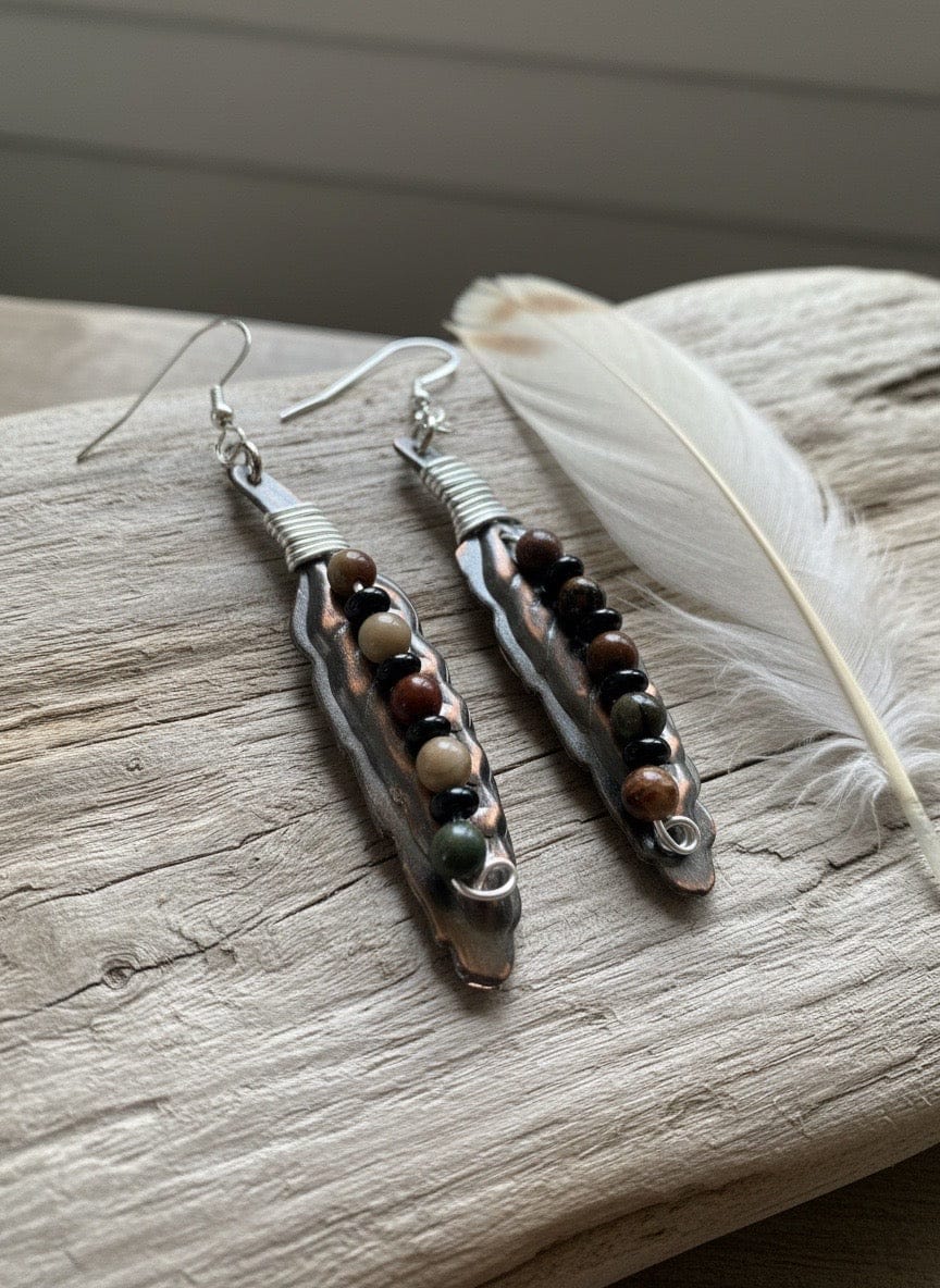 Pair of Copper earrings with beads on a wooden surface with a feather