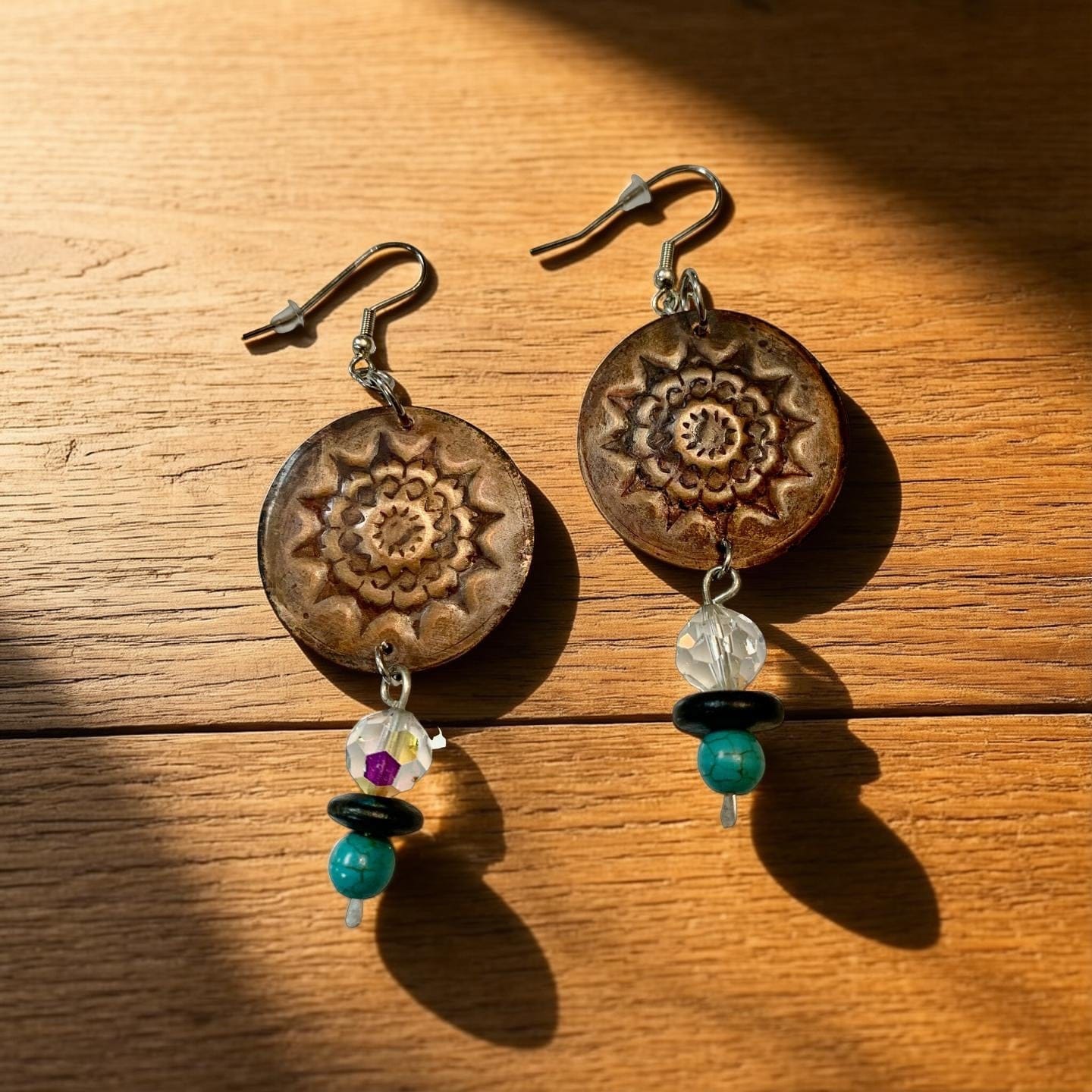 Pair of  copper earrings with mandala design on a wooden surface