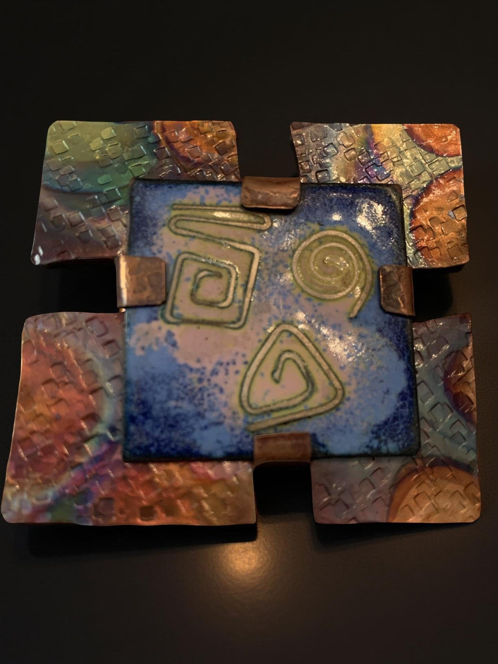 Decorative enamel brooch with abstract designs on a dark background 