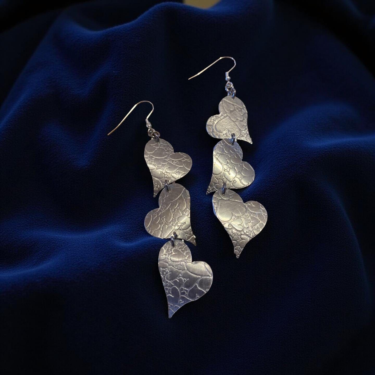 Silver heart-shaped  aluminum earrings on a dark blue fabric background