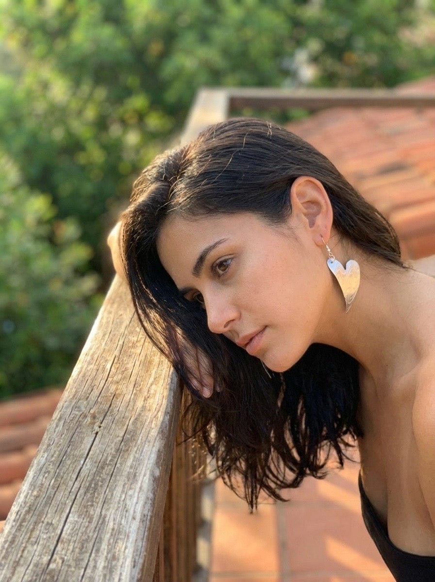 Woman with heart-shaped earrings leaning against a wooden railing outdoors