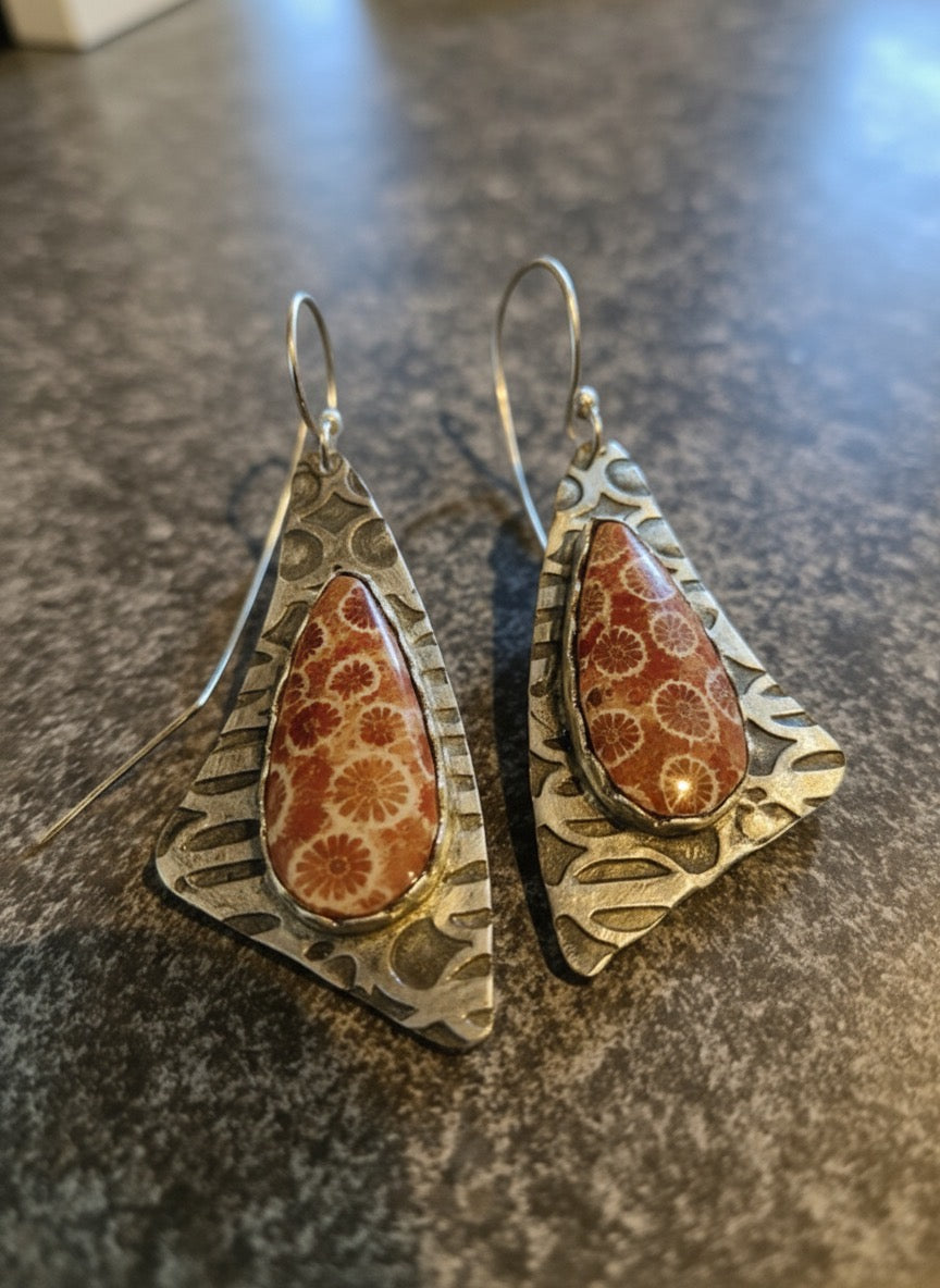 Pair of silver earrings with reddish tan stones on a dark surface