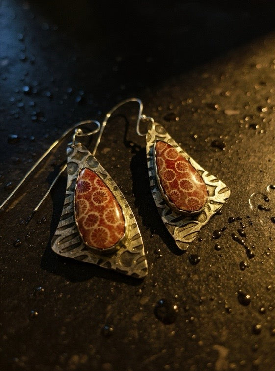 Pair of earrings with intricate fossil coral designs on a dark surface